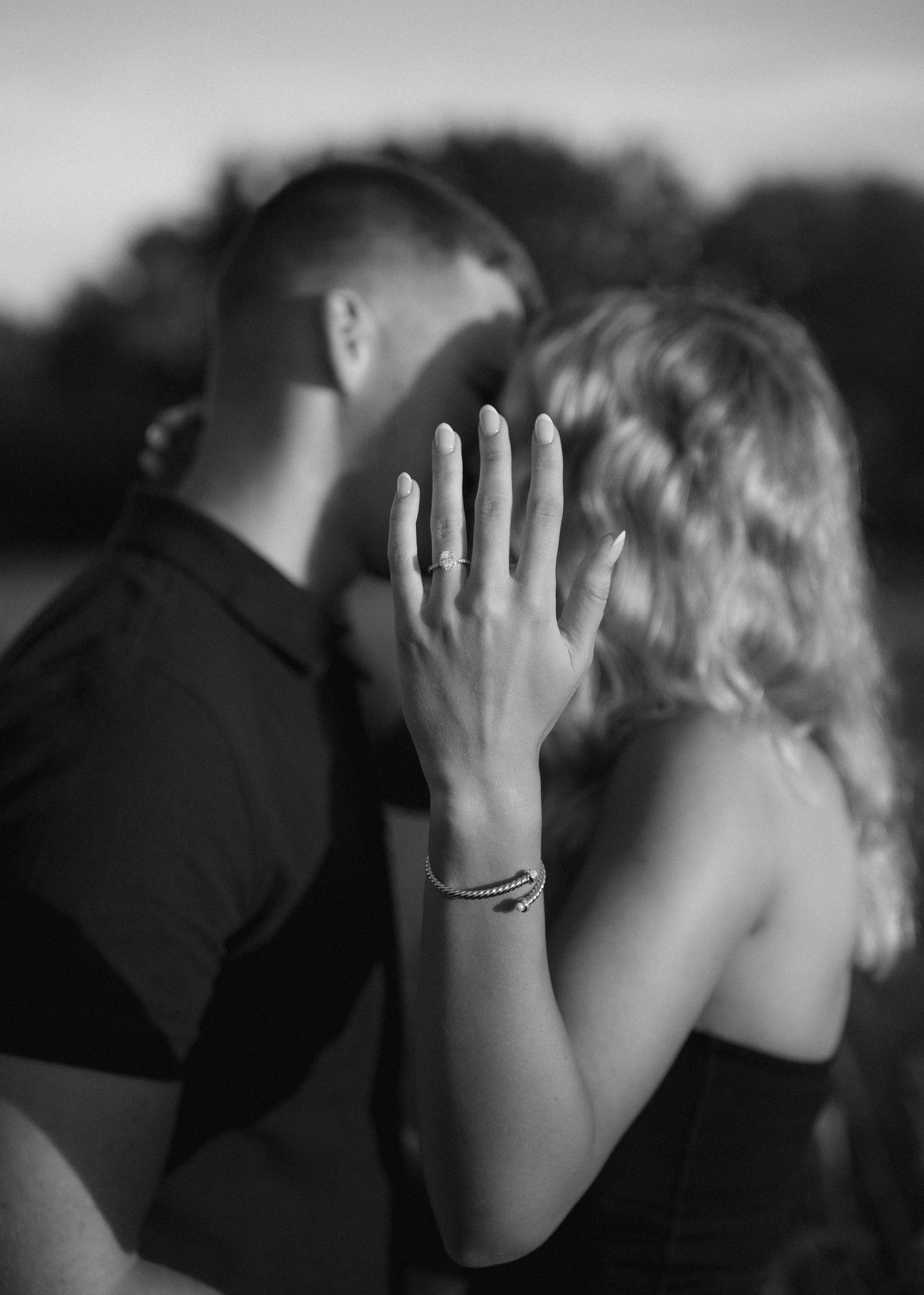 Black and white photo of an engaged couple nearly kissing as the woman shows off her diamond engagement ring.