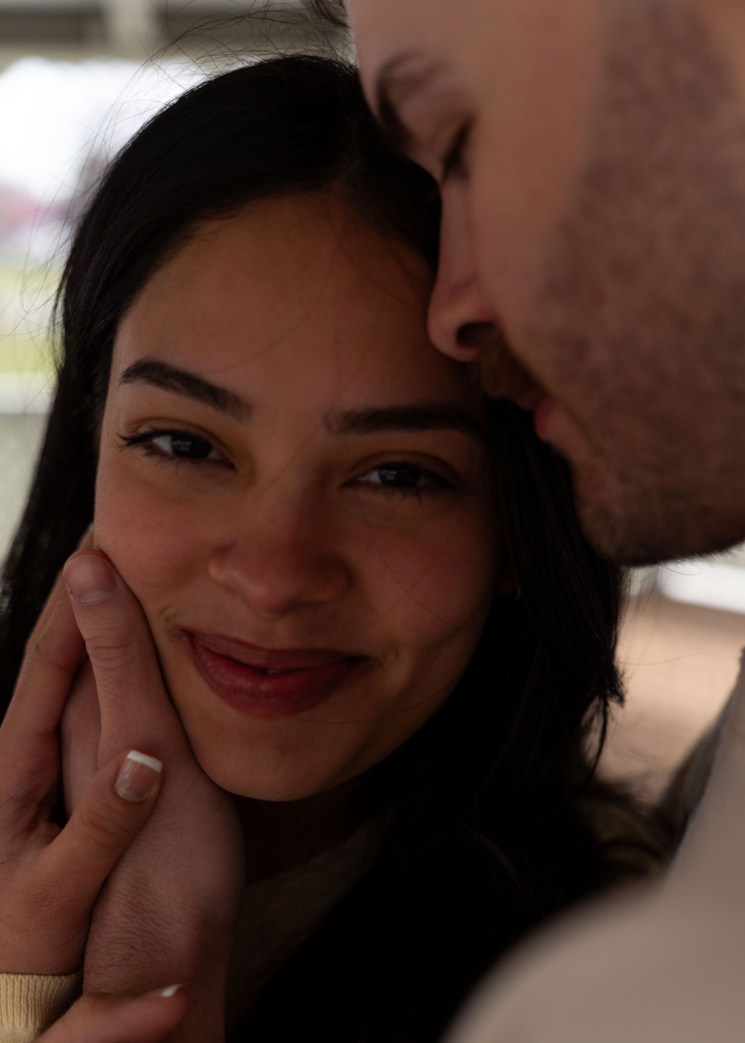 Woman smiling warmly as man kisses her cheek in a tender romantic moment.