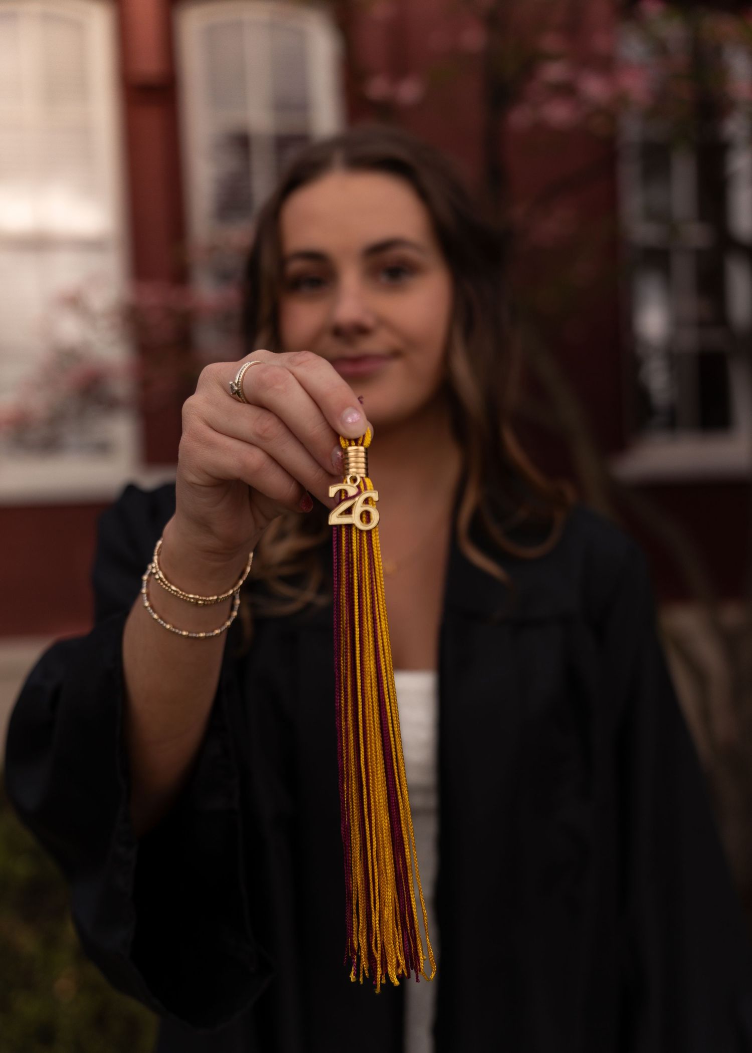 Graduate holding gold tassel with 26 charm for class of 2026 graduation photos.