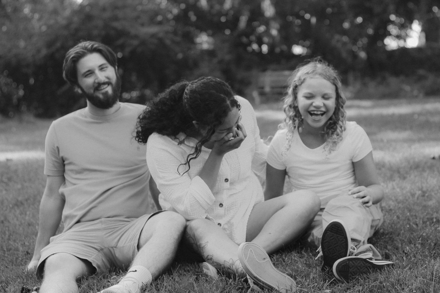 Black and white image of a cheerful family sitting on grass laughing together outdoors.