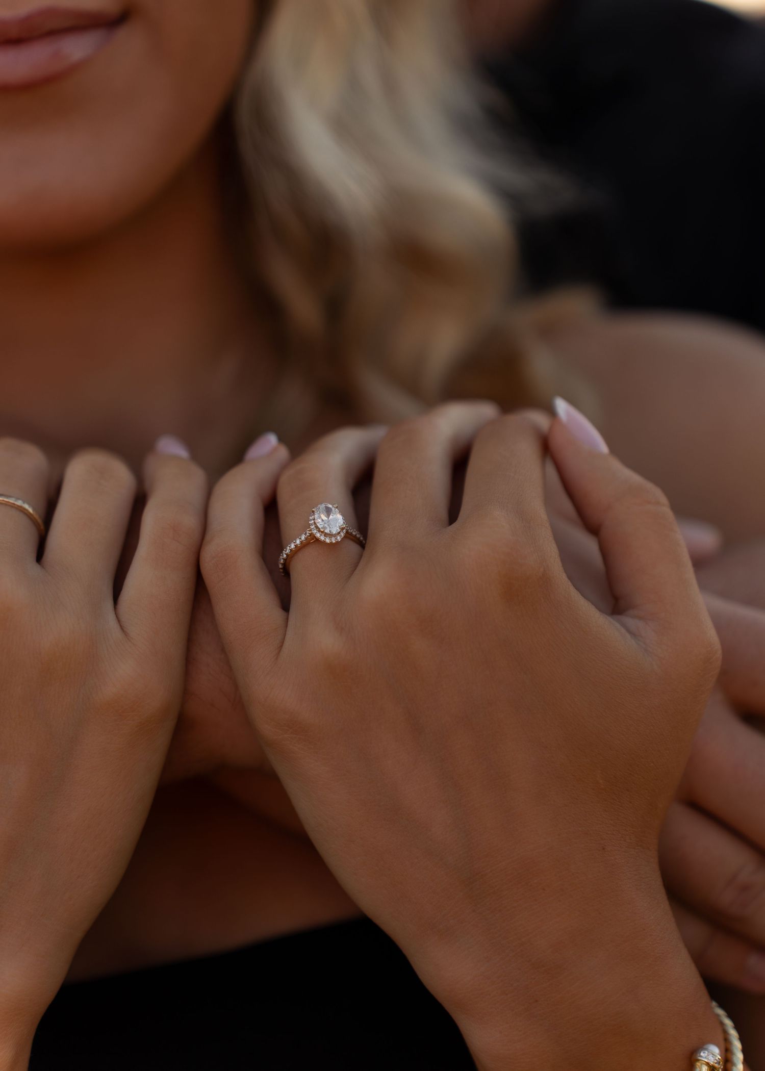 Close-up of a woman's hand displaying a stunning halo diamond engagement ring while embraced by her partner.