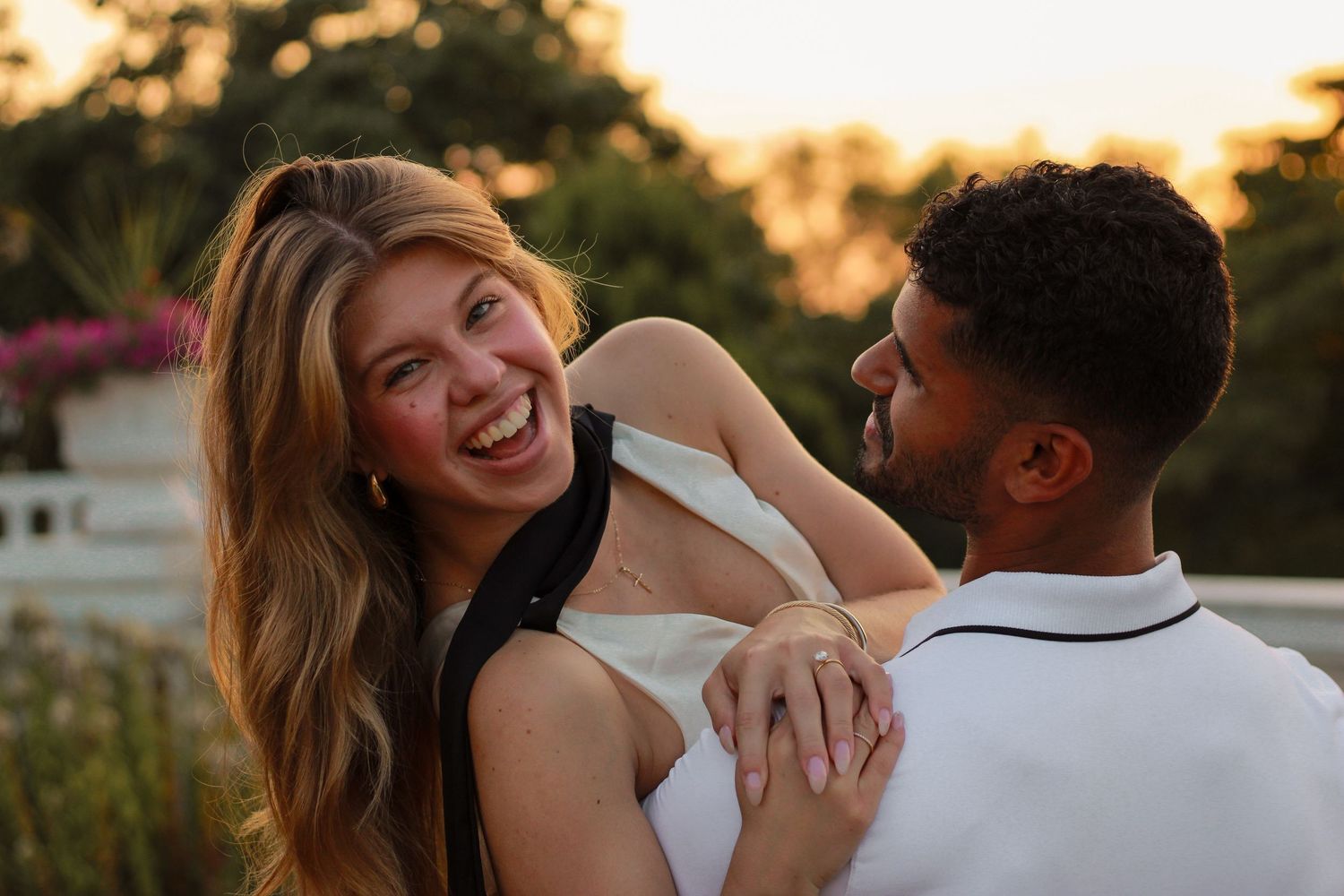 Laughing woman being held by her partner outdoors during a warm sunset engagement session.