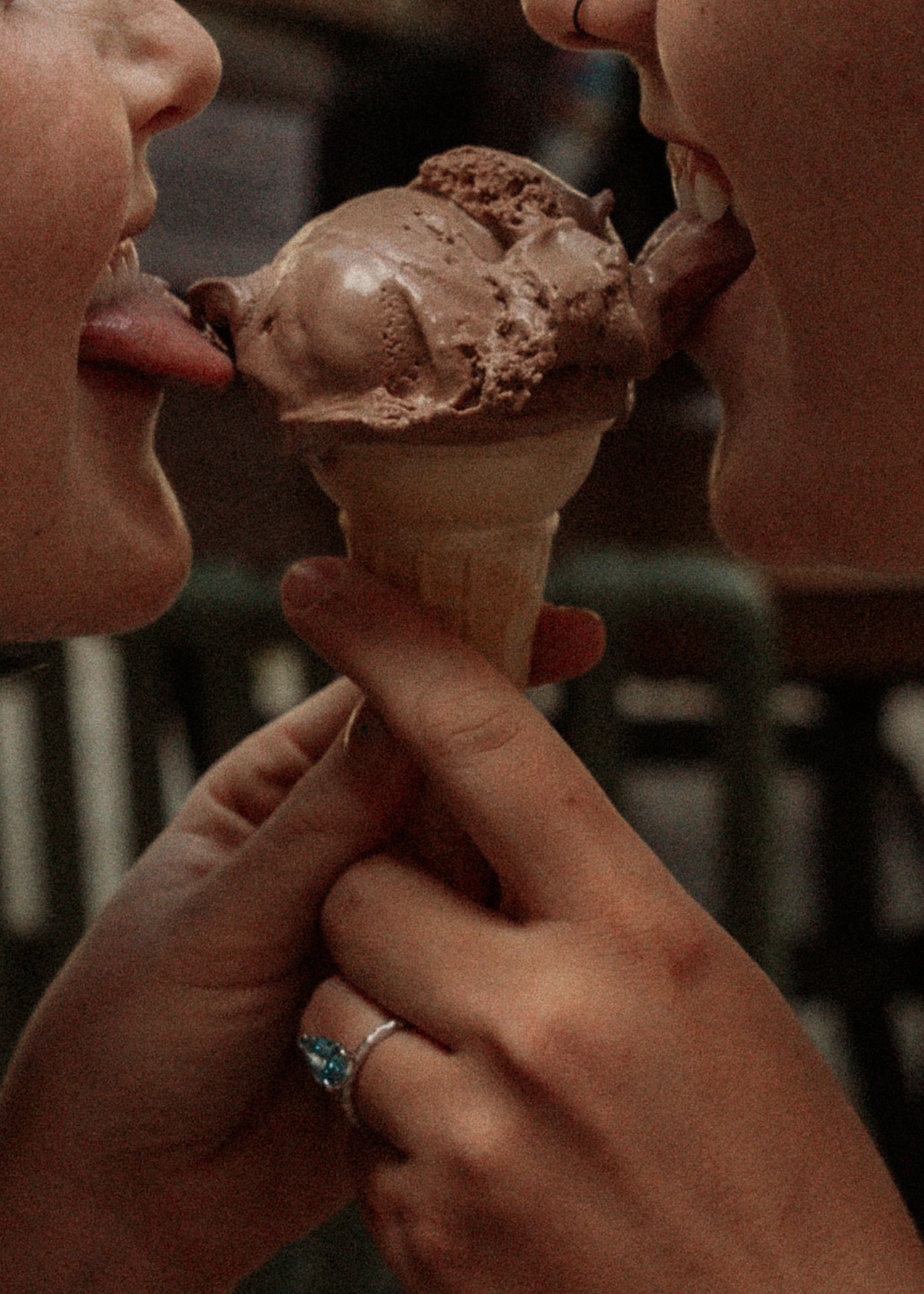 Couple sharing a chocolate ice cream cone, one wearing a ring, romantic moment.