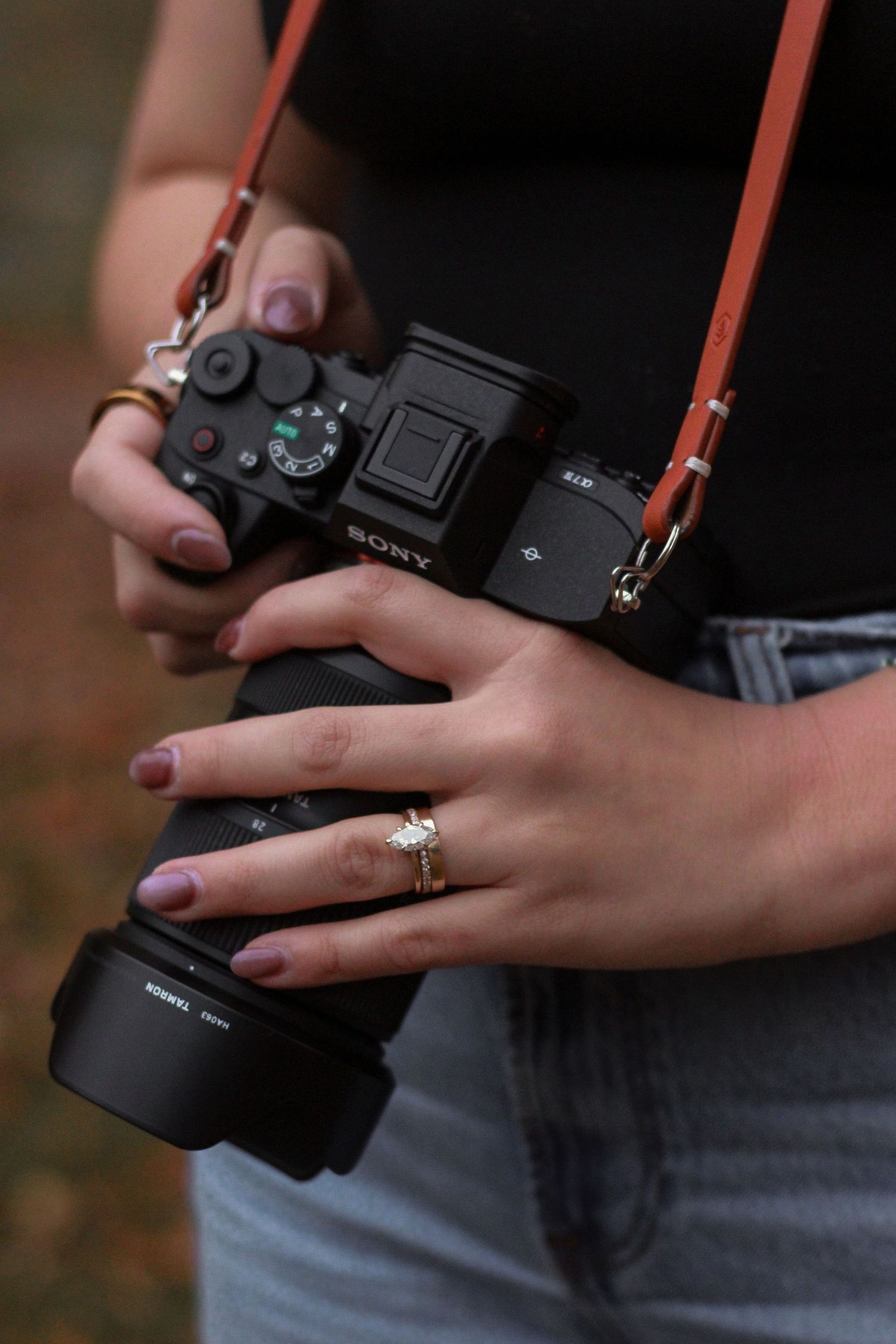 Close-up of a woman holding a Sony mirrorless camera with an engagement ring on her finger.