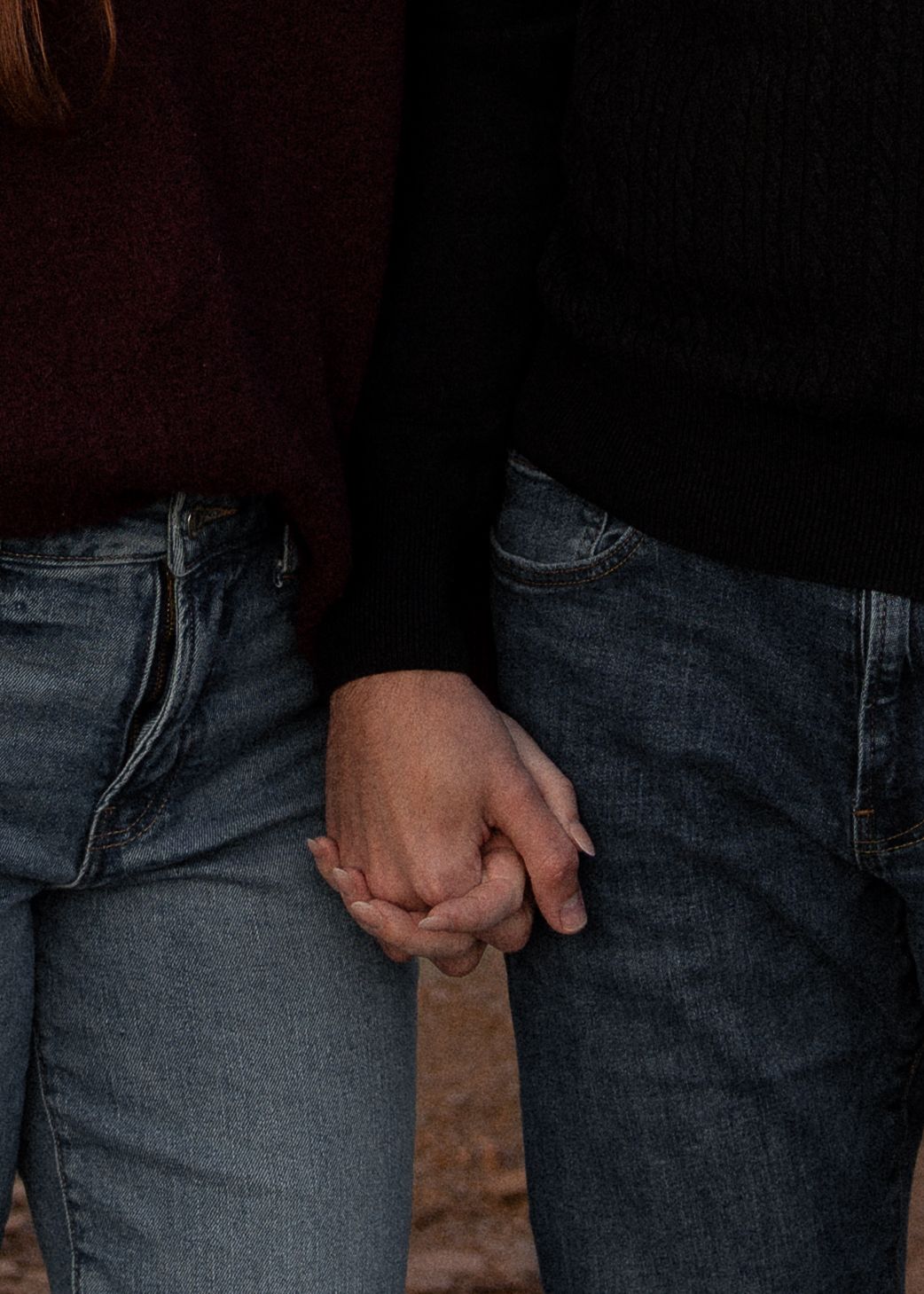 Close-up of couple holding hands wearing jeans during fall engagement photo session.