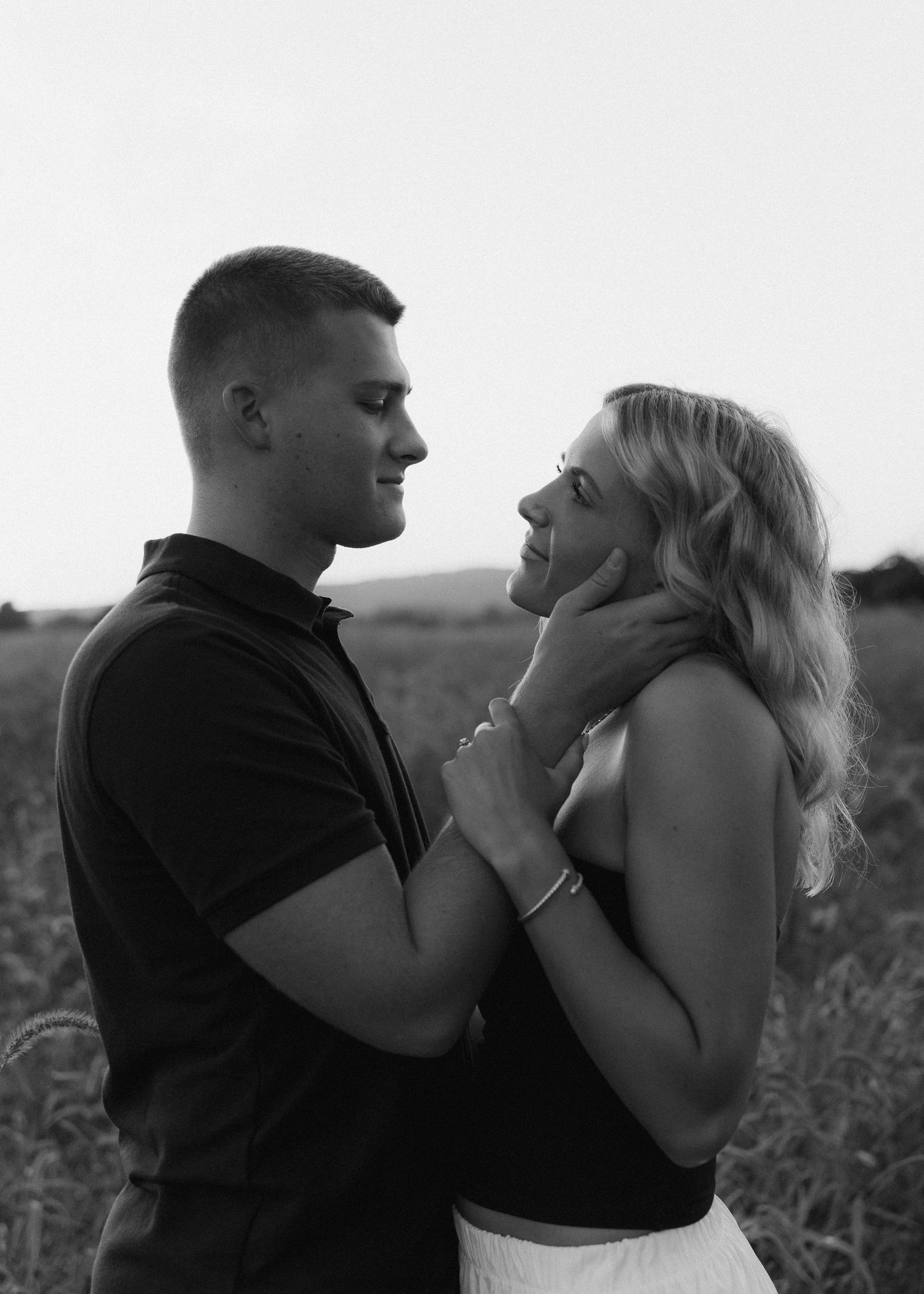 Black and white portrait of a couple gazing lovingly at each other in an open field at dusk.