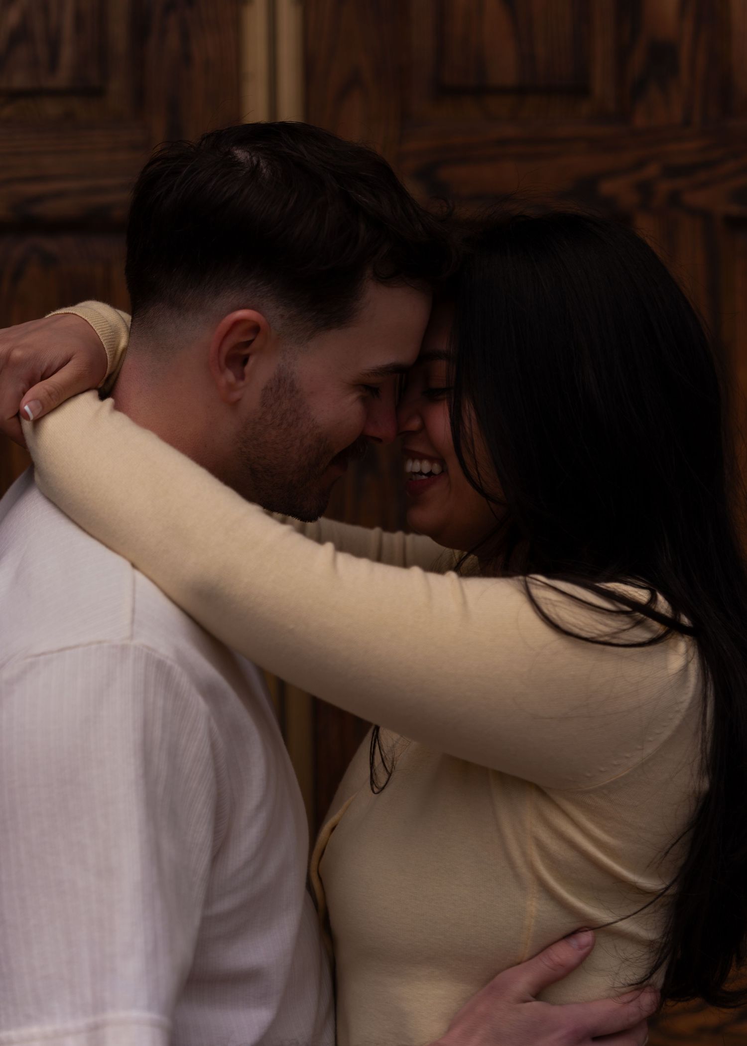 Joyful couple embracing and laughing together in front of a wooden door.