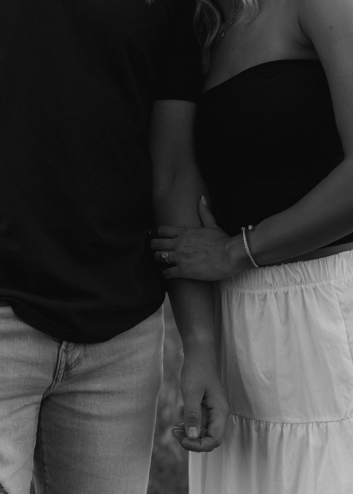 Black and white close-up of an engaged couple holding hands, showcasing her diamond engagement ring.