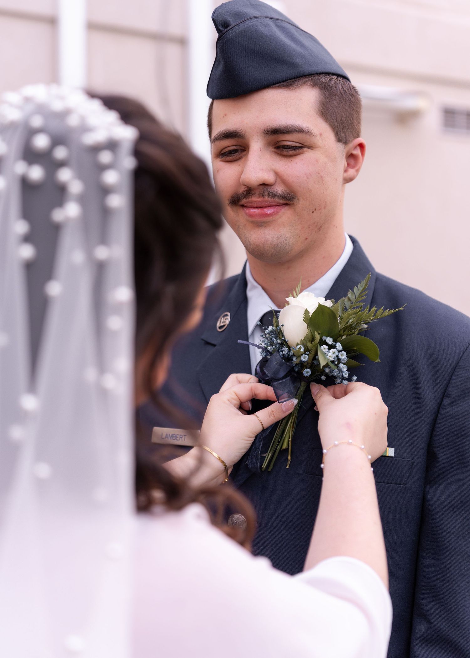 Bride pinning a white rose boutonniere on a smiling groom in Air Force dress uniform at wedding.