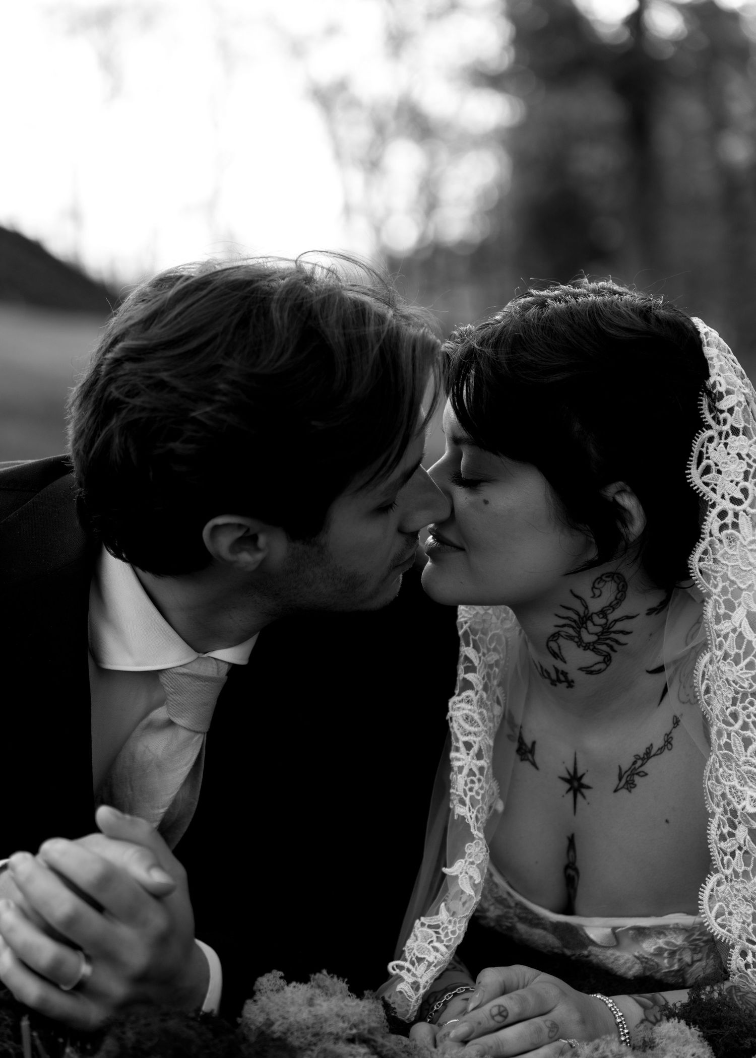 Tattooed bride and groom sharing first kiss in black and white wedding portrait outdoors.