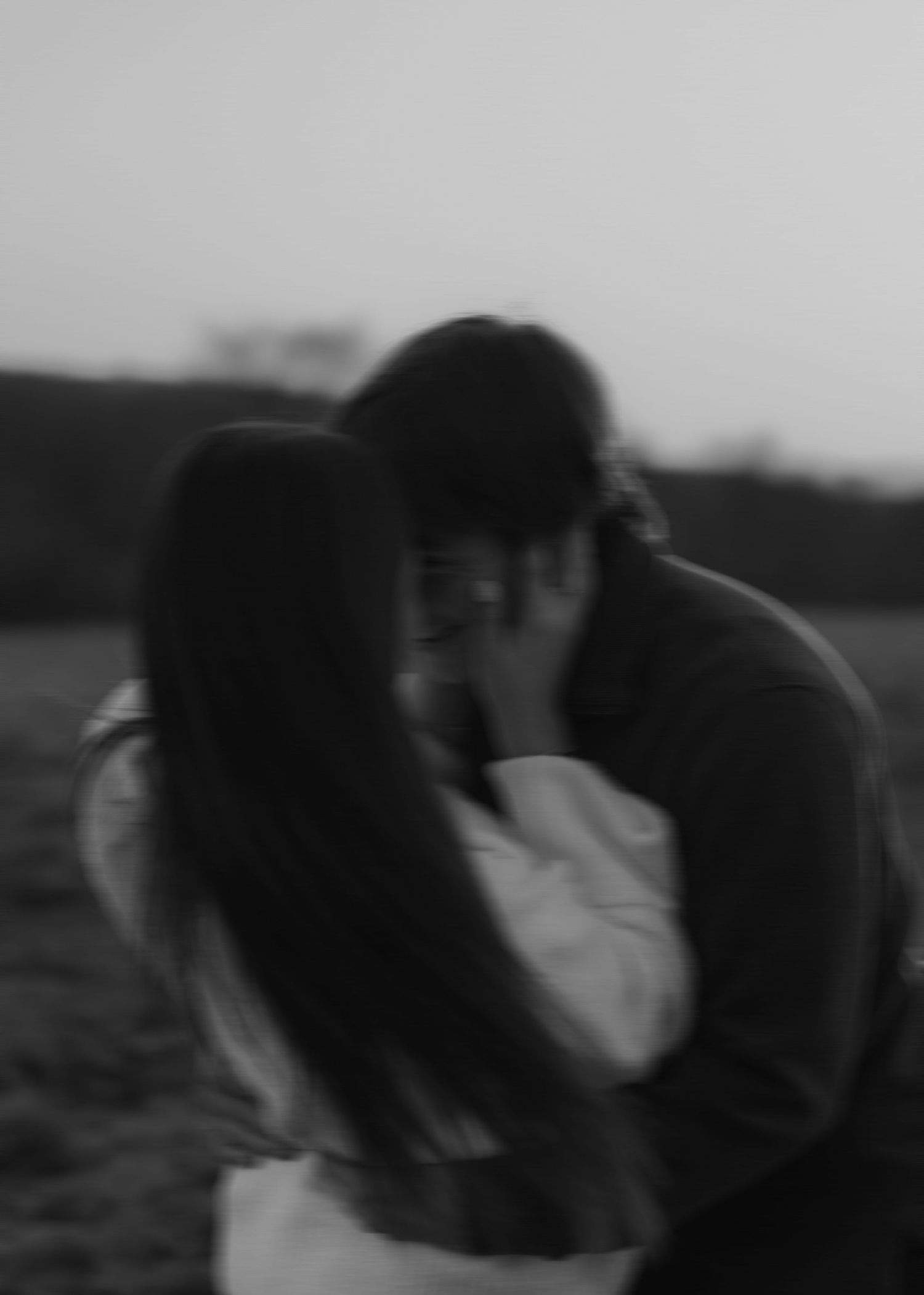 Black and white photo of couple sharing a passionate kiss outdoors at dusk in an open field.