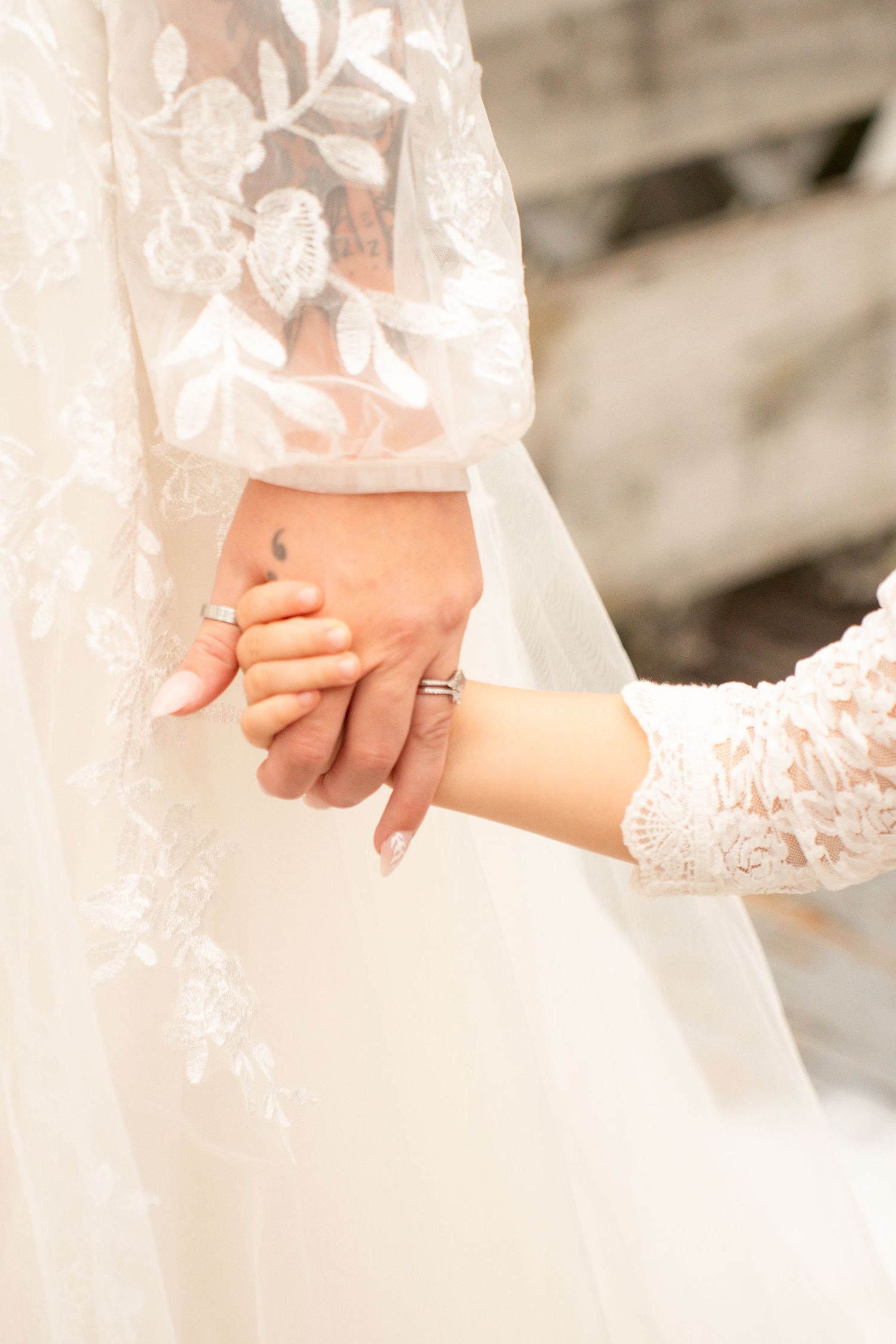 Bride and groom holding hands showing wedding rings in lace wedding attire.