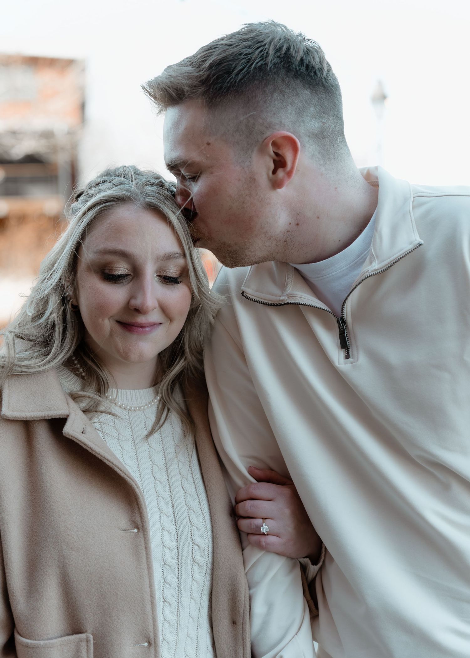 Man tenderly kissing woman on the forehead as she smiles softly during an engagement photo session.