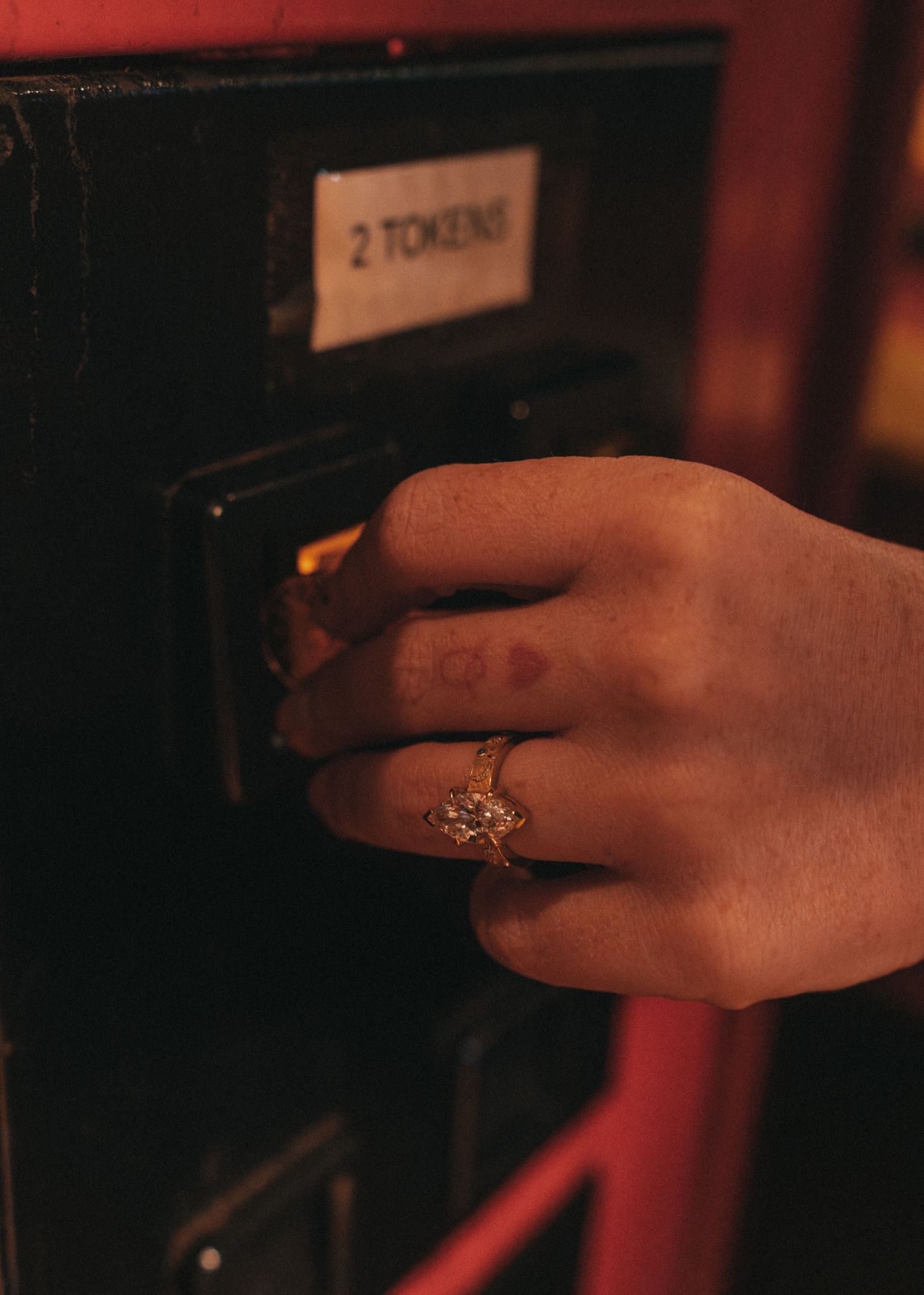 Close-up of hand with diamond engagement ring inserting token into arcade machine.