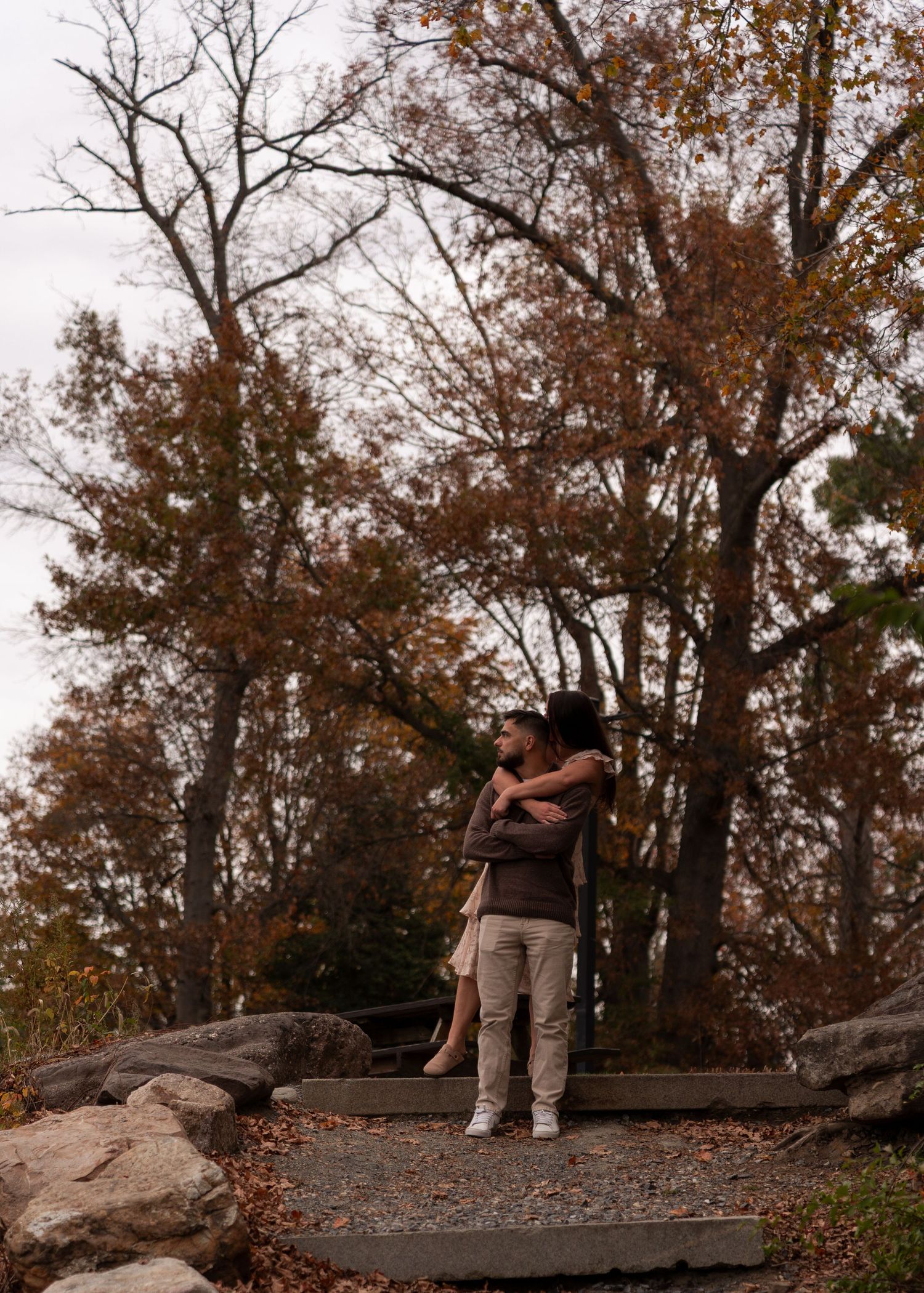 Couple embracing and kissing on a stone path surrounded by colorful autumn trees in a park.