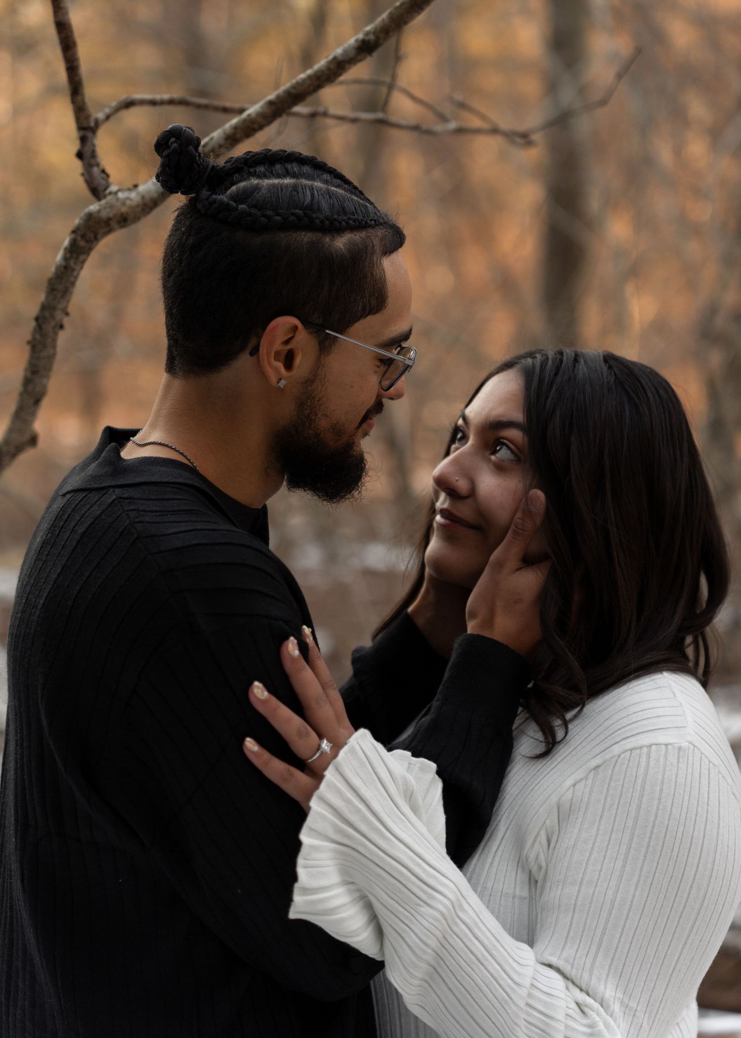 Couple sharing a tender moment in autumn woods, man gently touching womans face, wearing black and white sweaters.