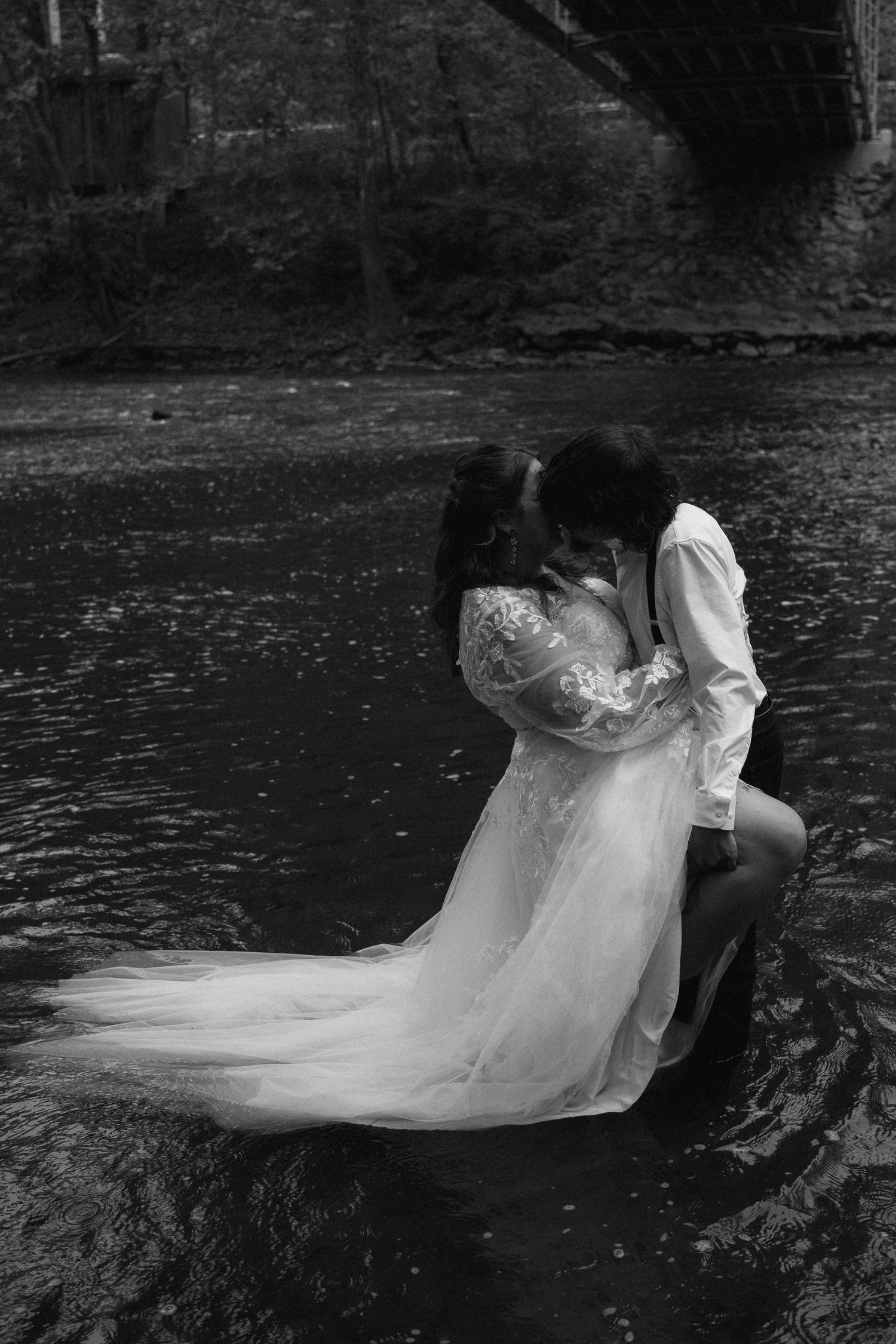 Bride and groom sharing romantic kiss while standing in river in black and white.