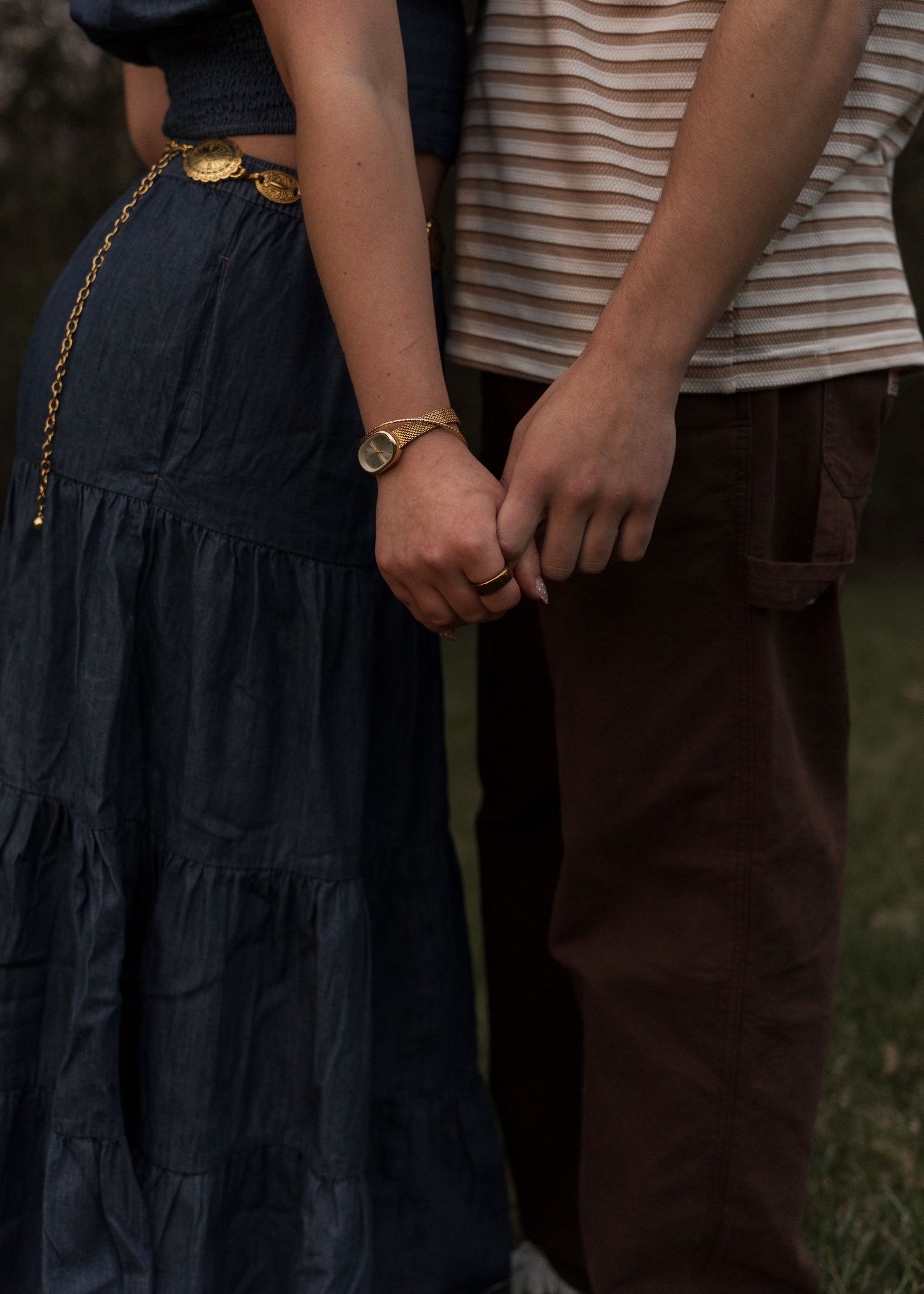 Close-up of couple holding hands, woman wearing navy tiered skirt and gold chain belt.