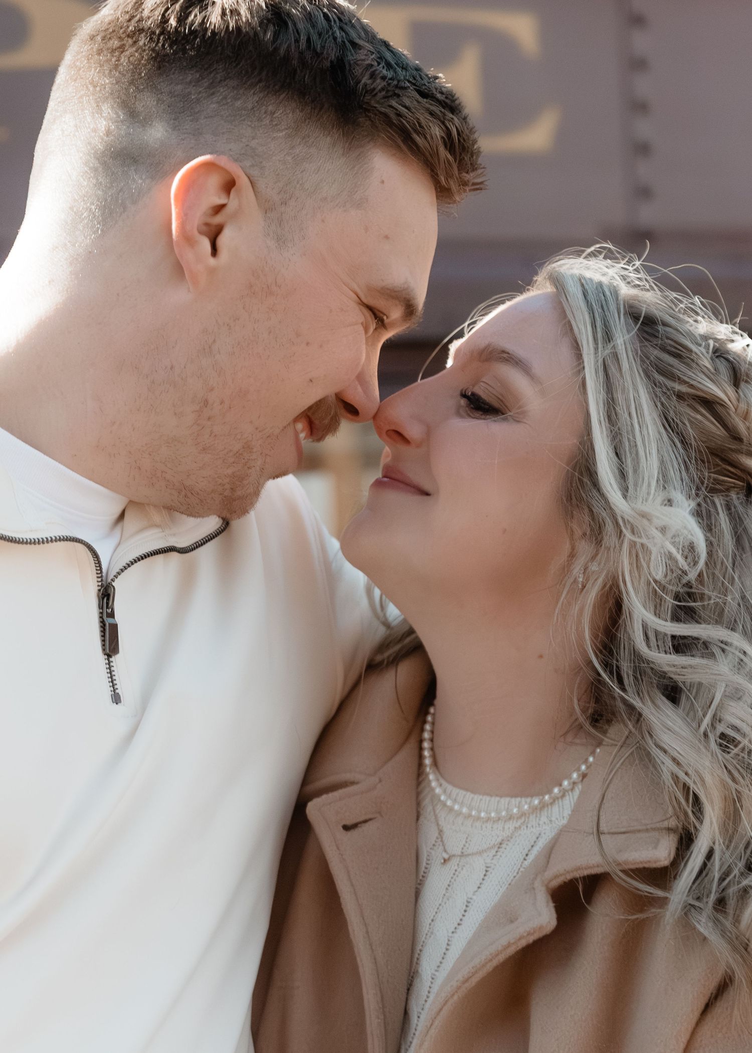 Couple sharing a romantic almost-kiss moment, woman wearing pearl necklace during golden hour engagement shoot.