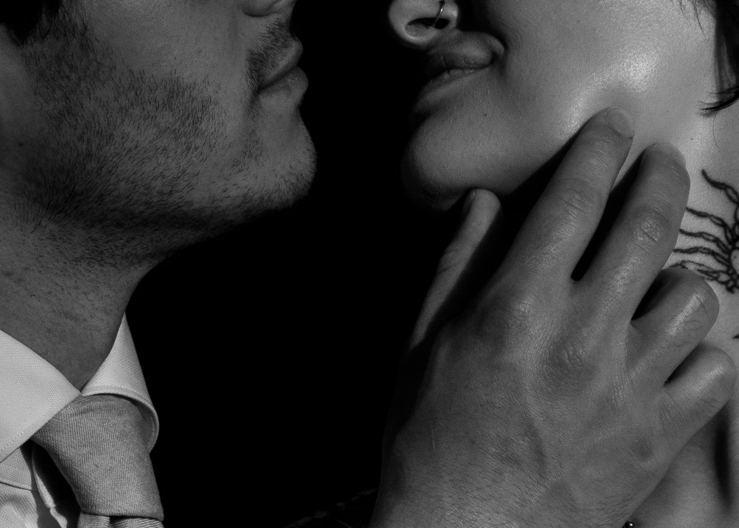 Black and white close-up of a romantic couple almost kissing, man gently holding woman's face.