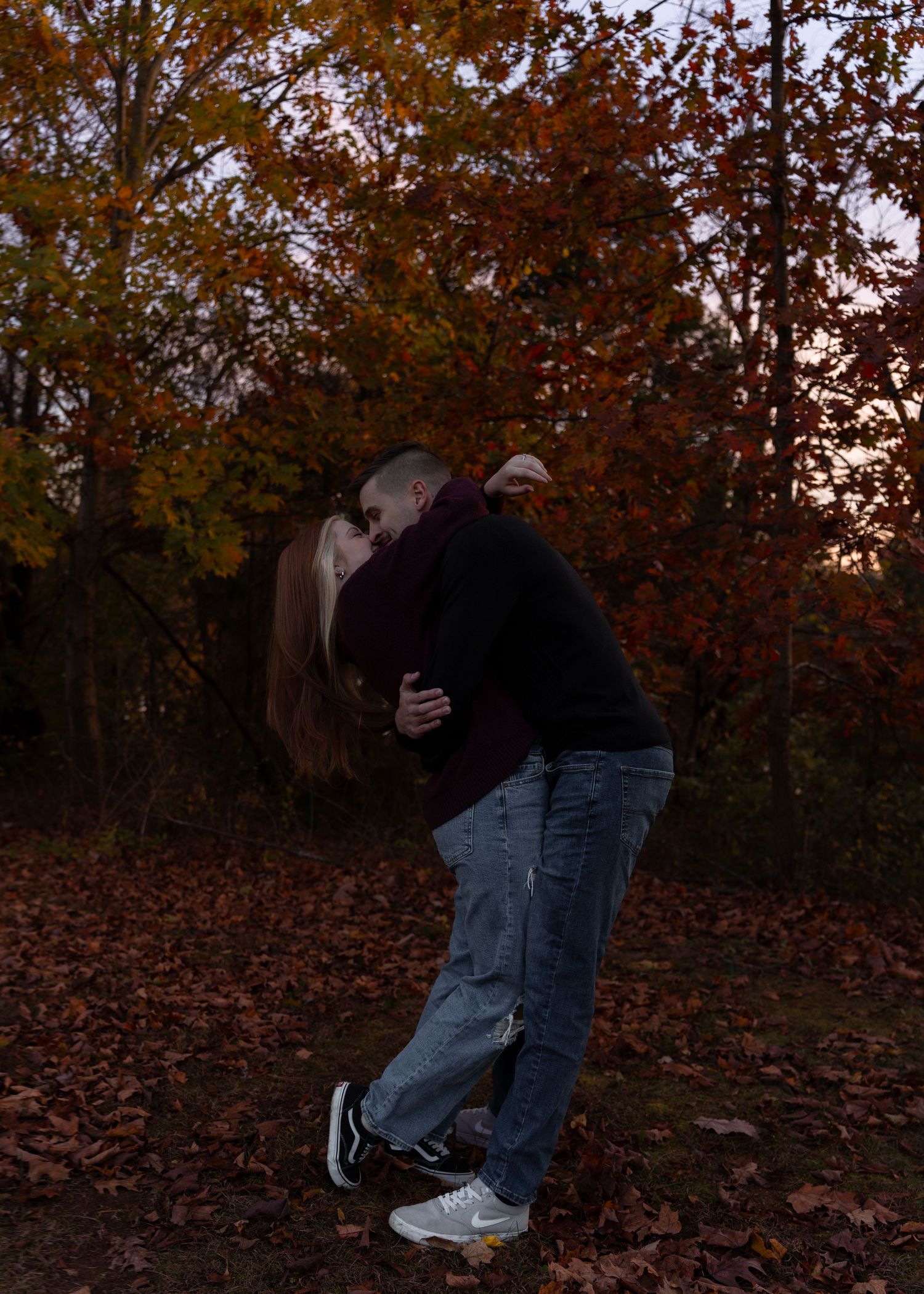 Couple sharing a romantic dip kiss surrounded by colorful autumn leaves in a wooded setting.