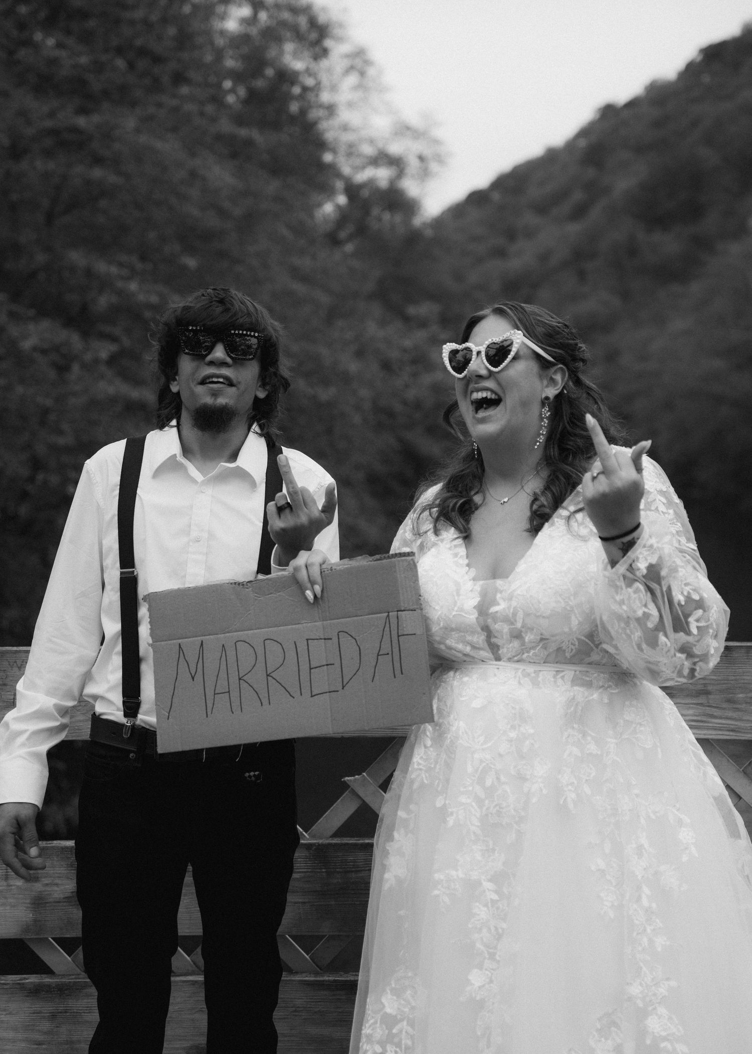 Newlyweds in black and white holding Married AF sign, wearing sunglasses and celebrating.