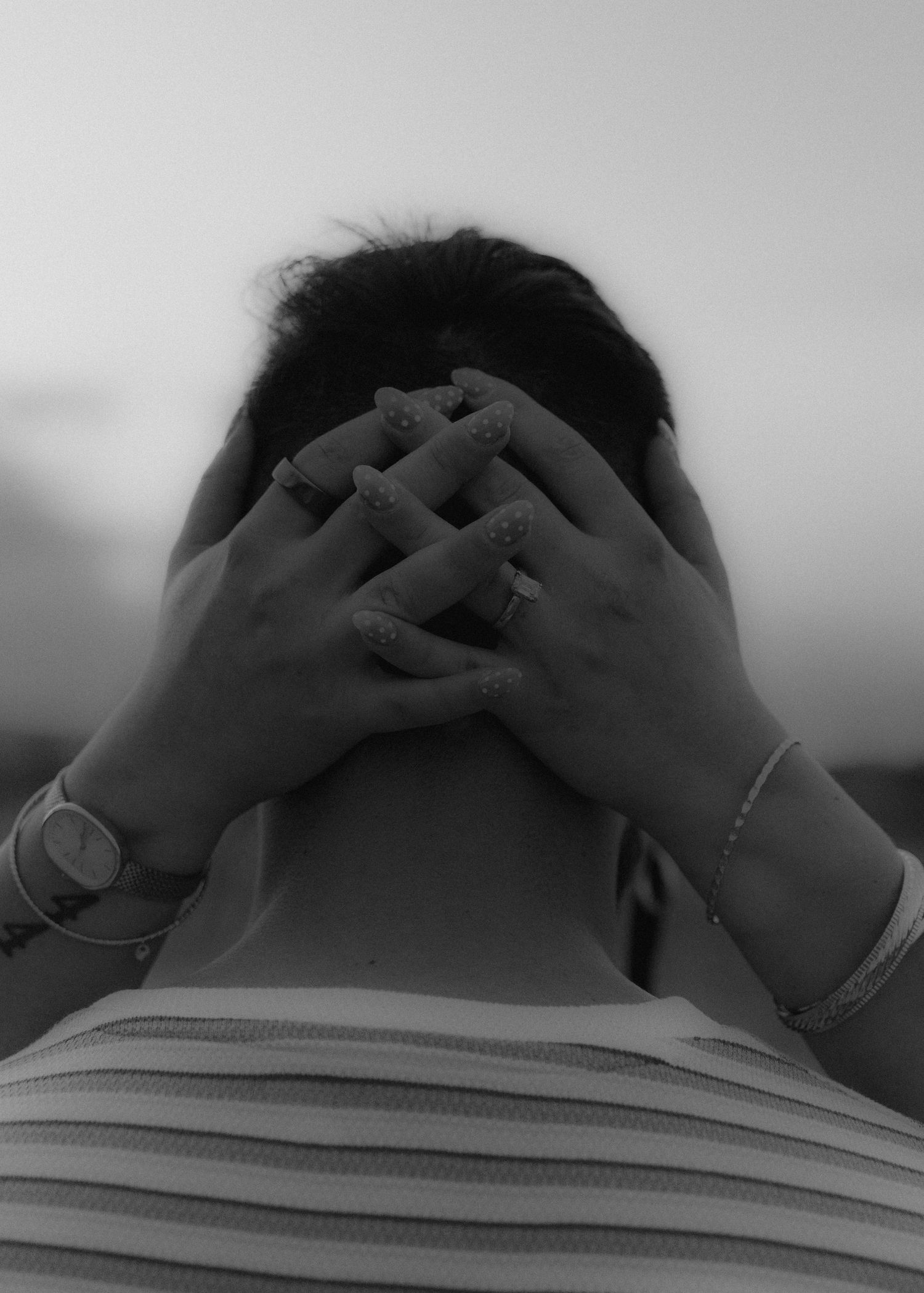 Black and white portrait of woman covering face with both hands wearing bracelet and watch.