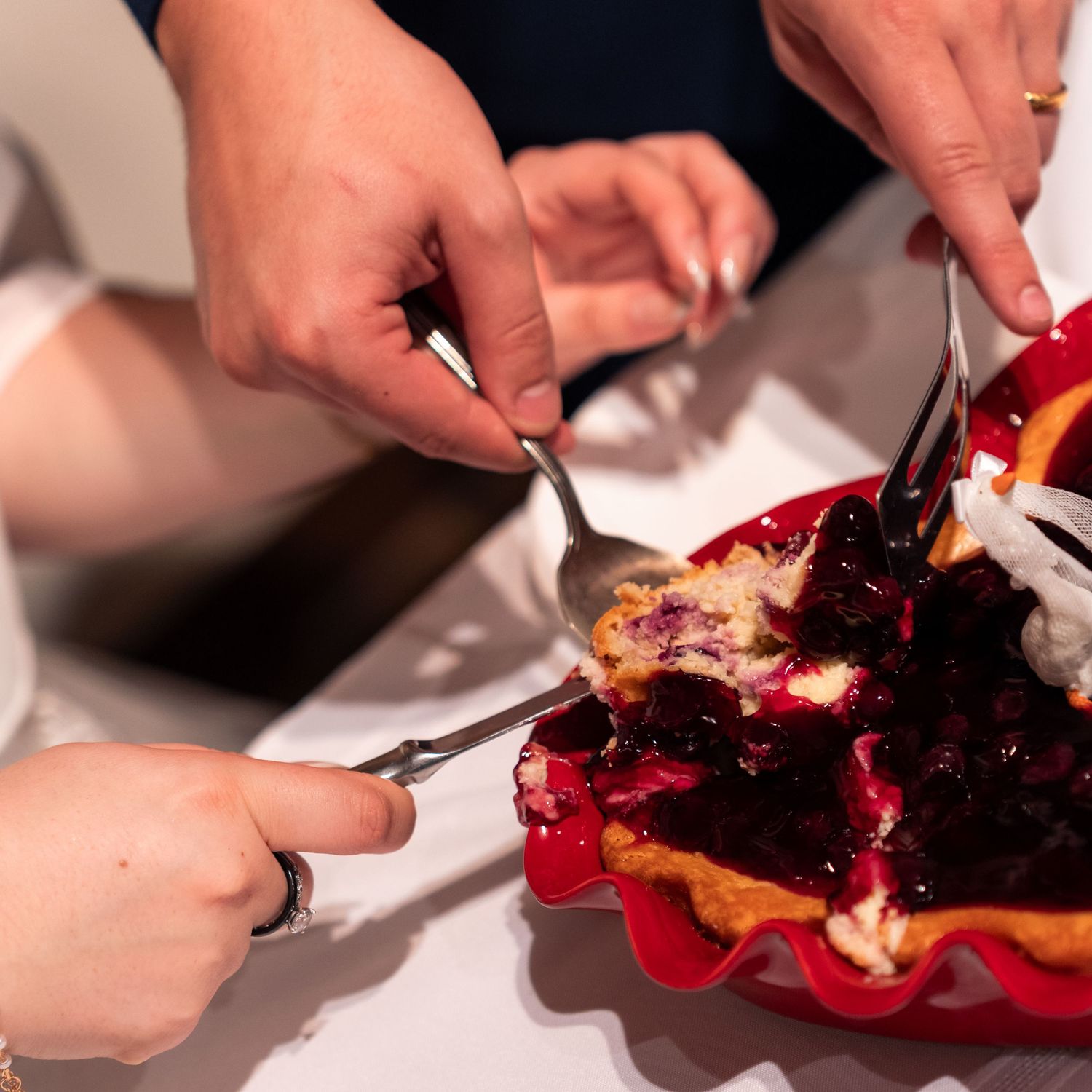 Hands serving slices of blueberry cheesecake at a wedding reception dessert table.