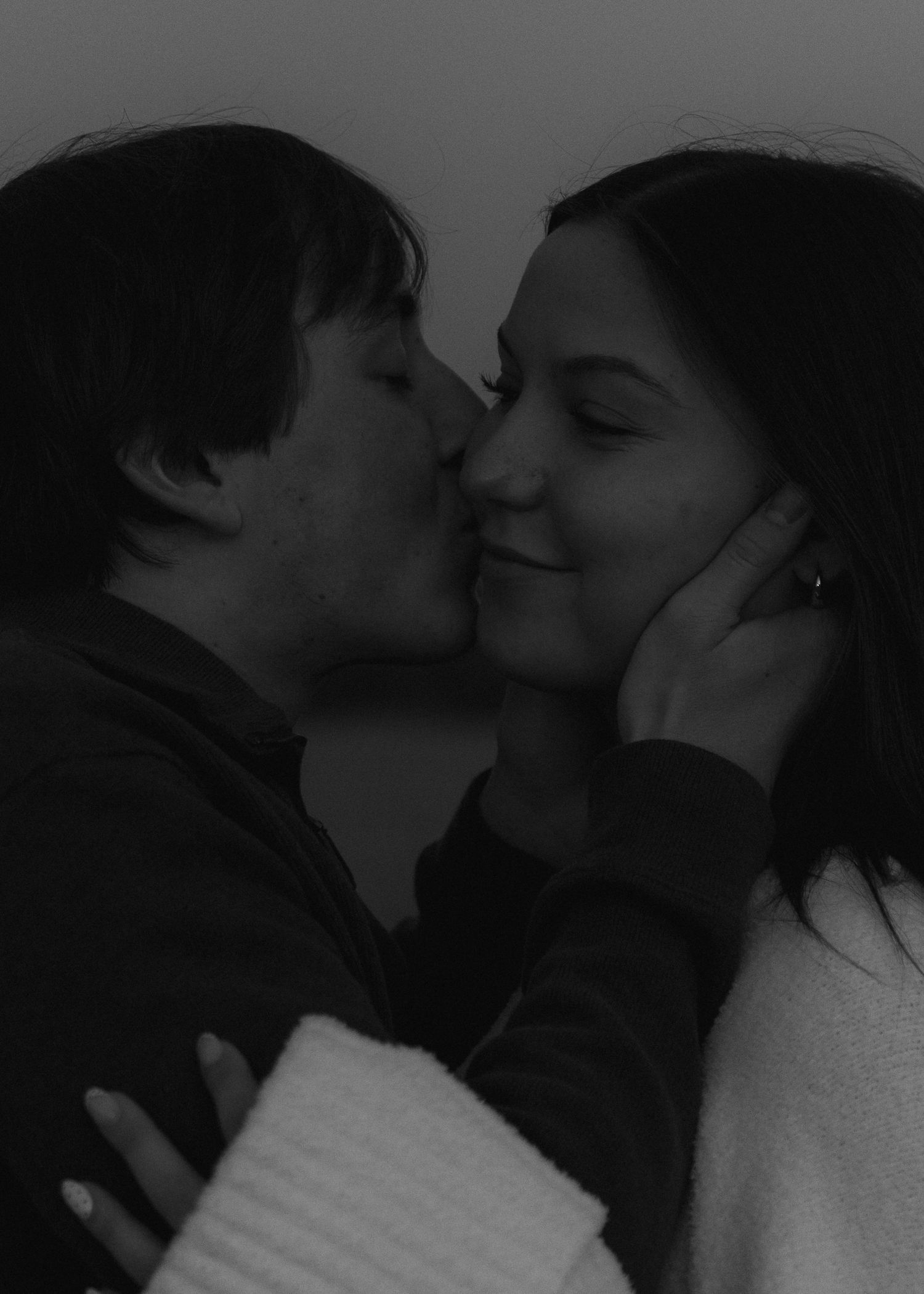 Black and white photo of man kissing smiling woman on the cheek during a romantic couples session.