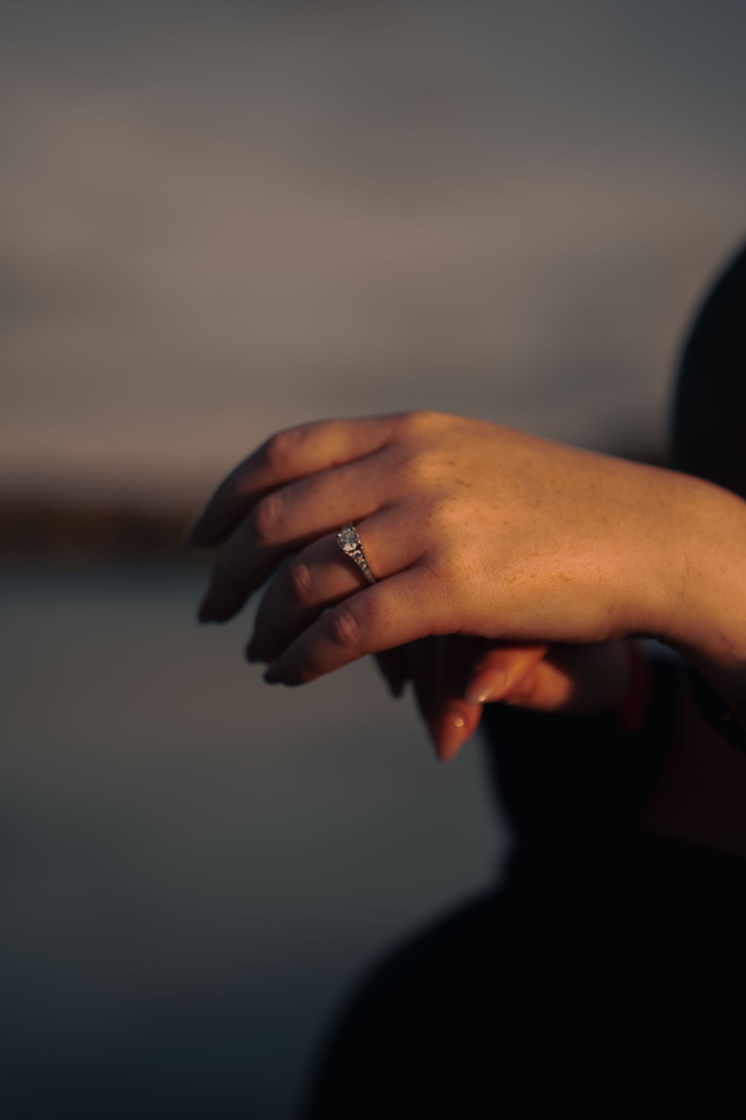 Close-up of a womans hand displaying a sparkling diamond engagement ring in soft evening light.