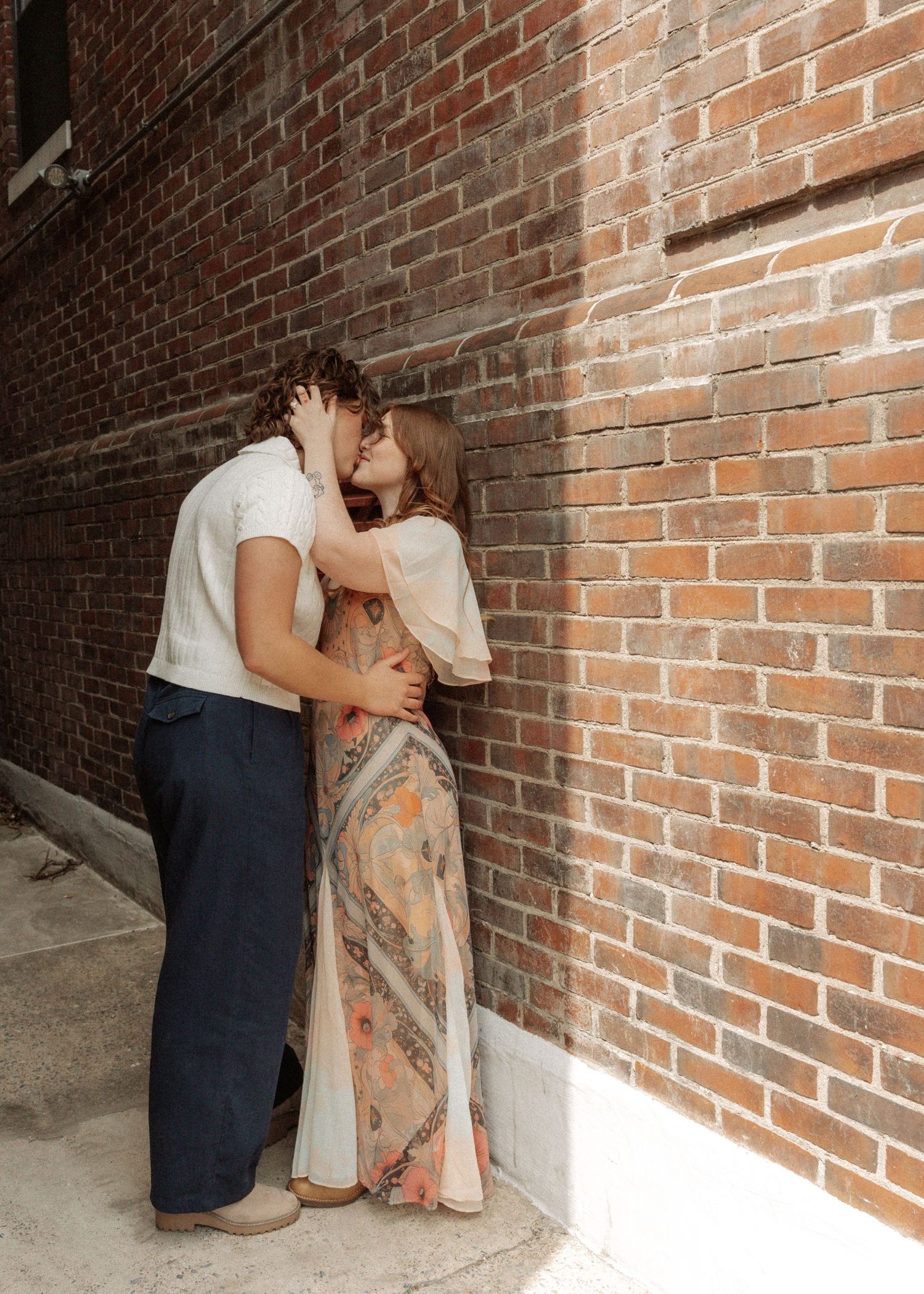 Couple sharing a passionate kiss against rustic brick wall in urban alleyway.