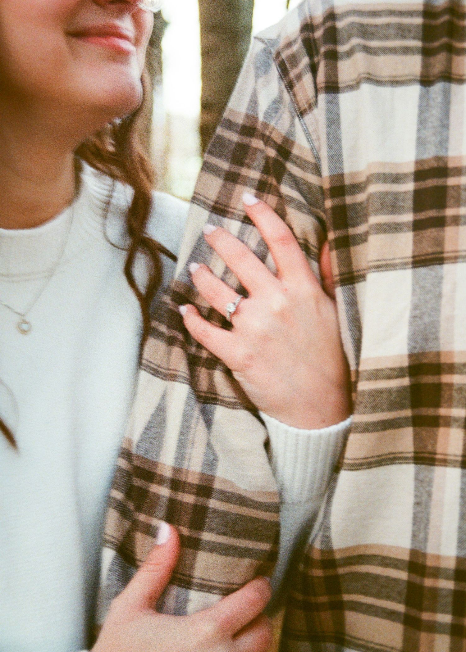 Close-up of woman's hand showing diamond engagement ring resting on man's plaid flannel shirt.