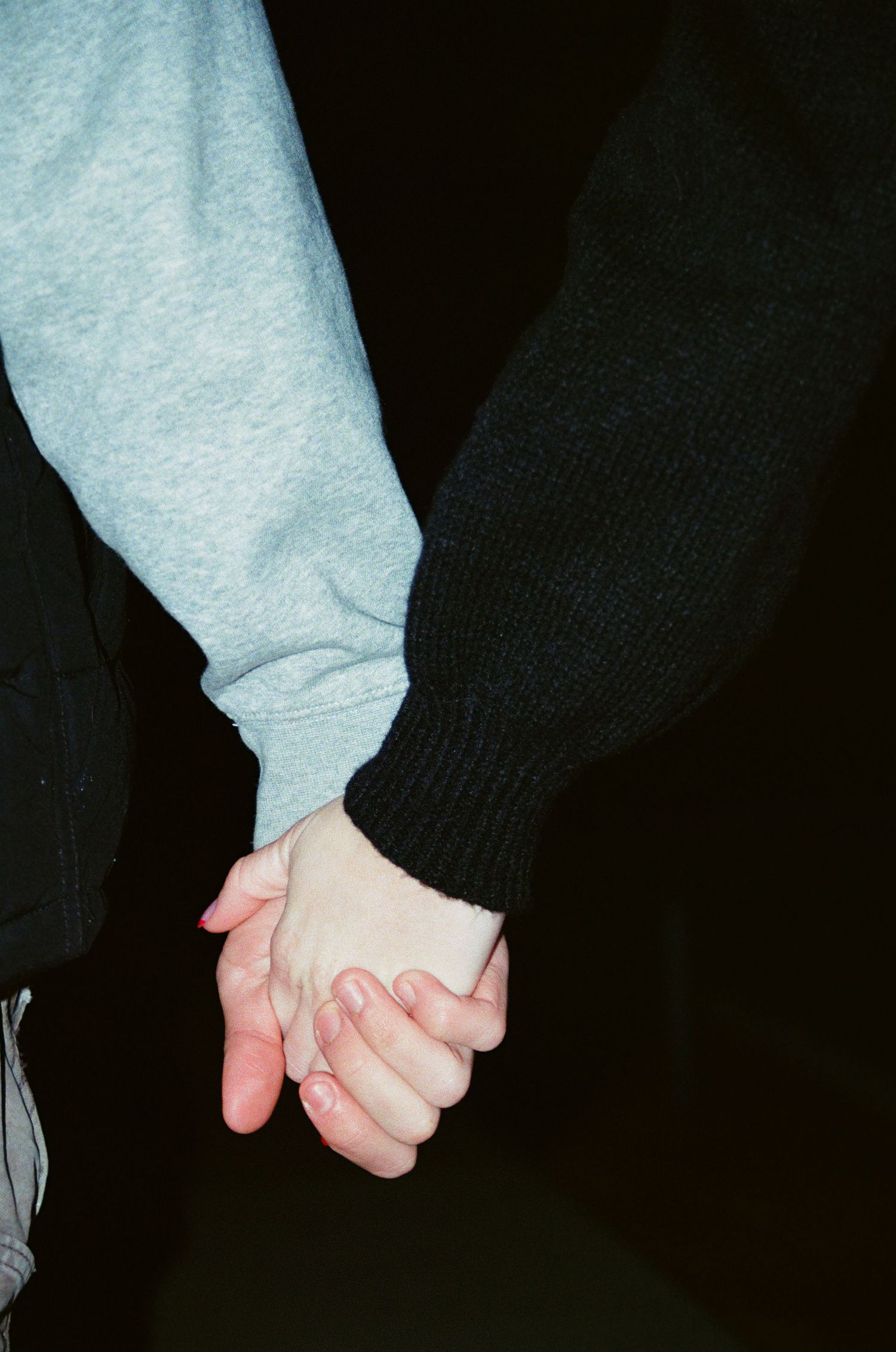 Close-up of couple holding hands at night, wearing light blue and dark knit sweater sleeves.