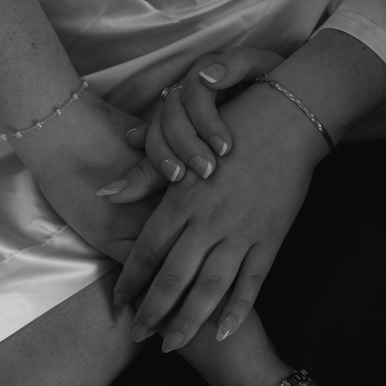 Black and white close-up of bride and bridesmaid holding hands with bracelets and rings.