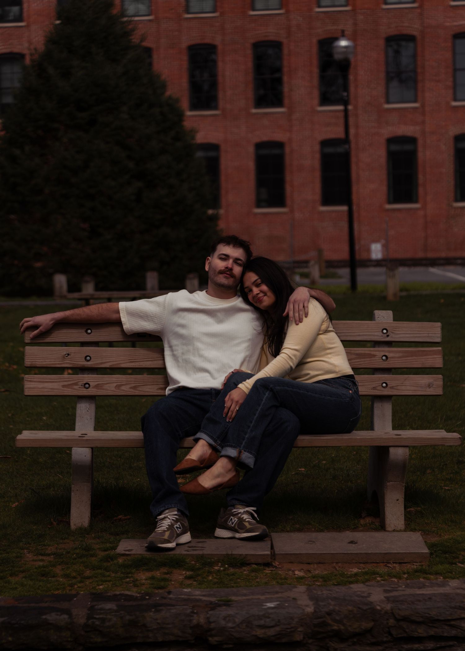 Happy couple sitting together on a park bench in front of a brick building.