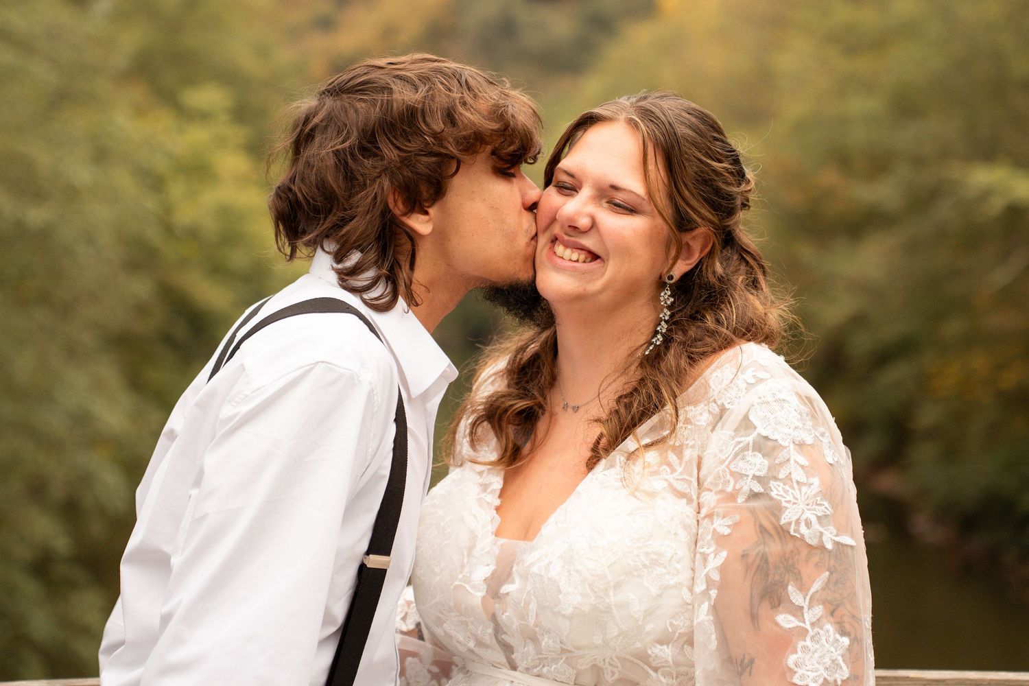 Groom kissing smiling bride on cheek during outdoor fall wedding portrait.