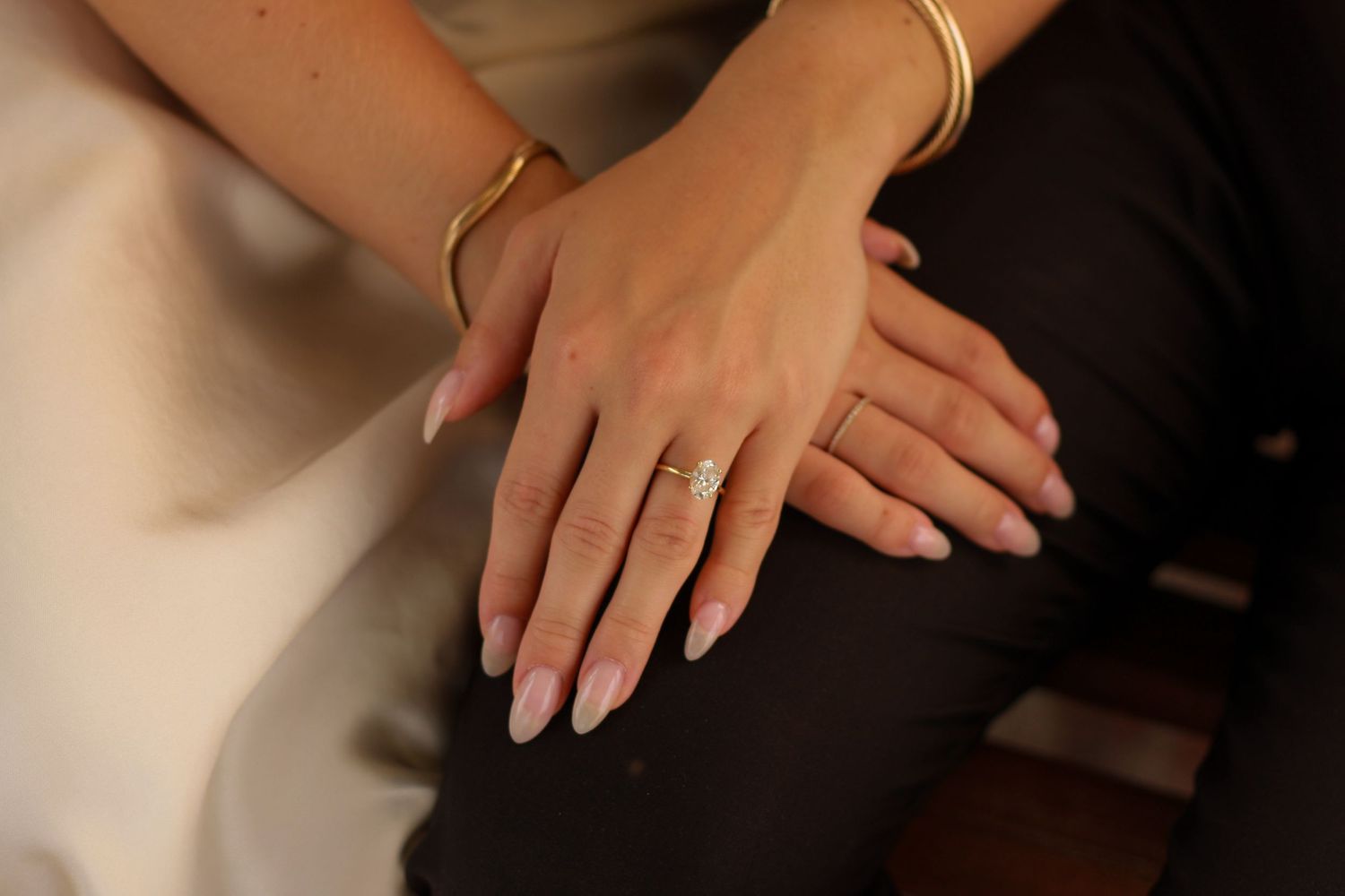 Close-up of an engaged couple's hands showing a diamond engagement ring and gold bracelet.