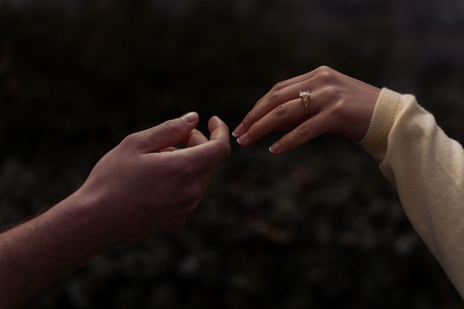 Close-up of two hands gently touching, woman wearing a delicate gold engagement ring.