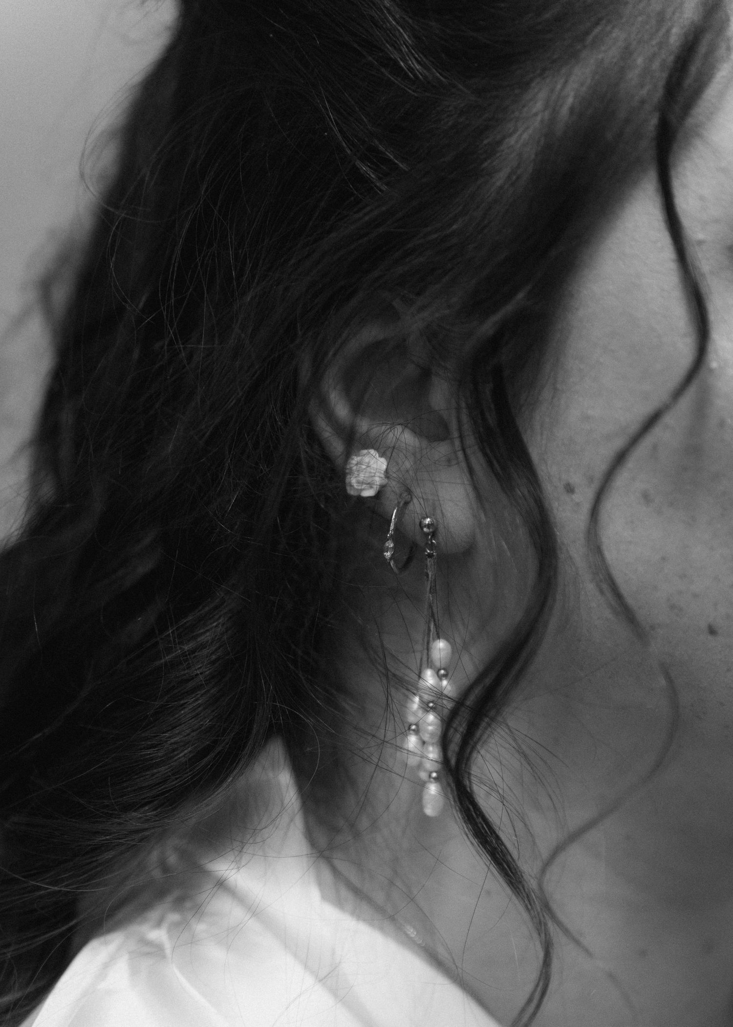 Close-up black and white photo of a bride wearing elegant pearl and rose drop earrings with dark wavy hair.