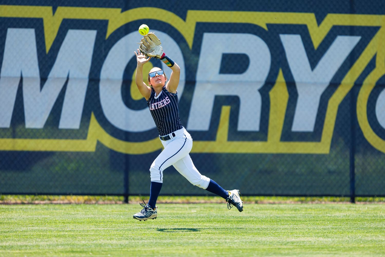 Softball player catching a fly ball in the outfield during a college game at Emory University.