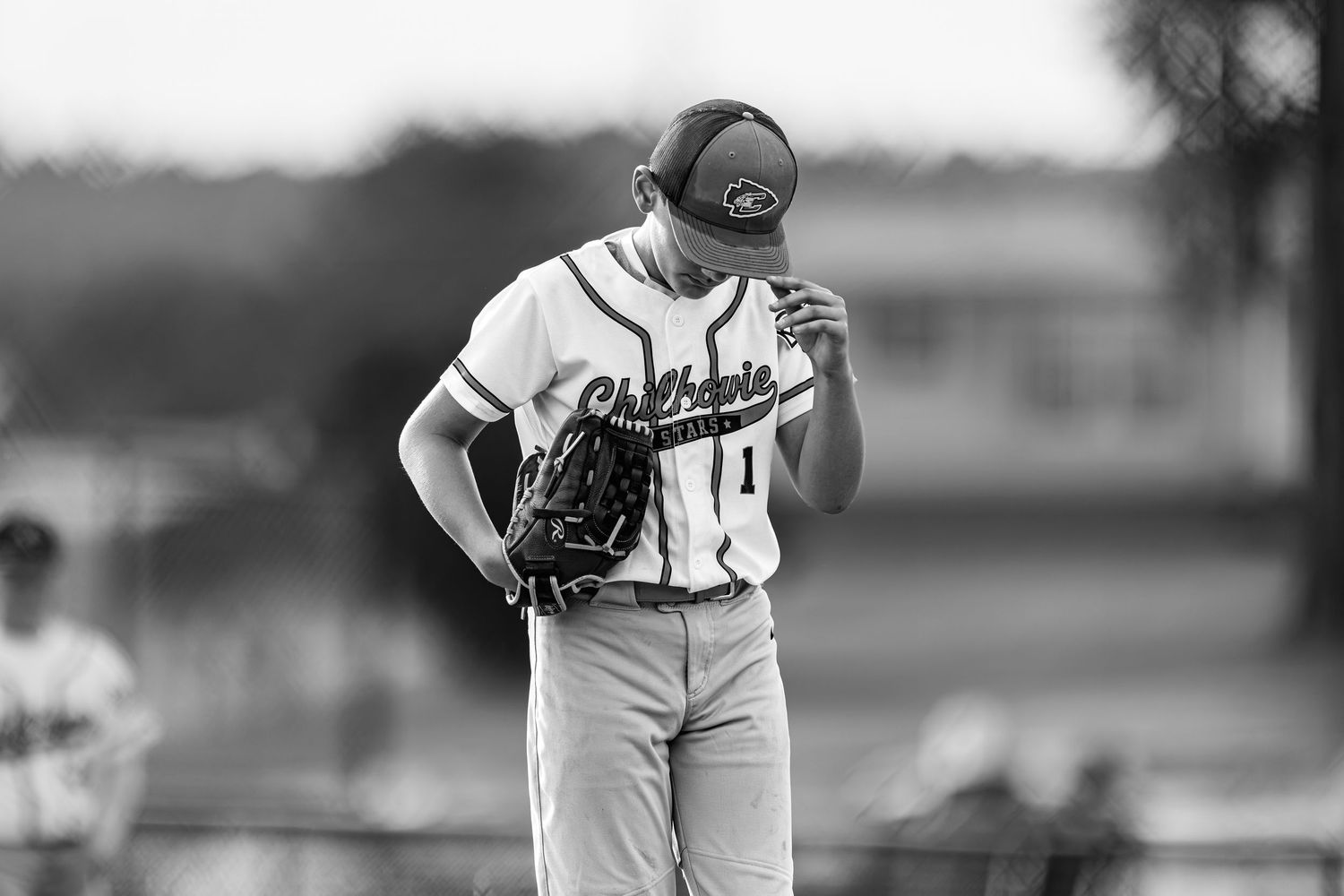 Black and white photo of a baseball pitcher in uniform holding his glove up on the mound.