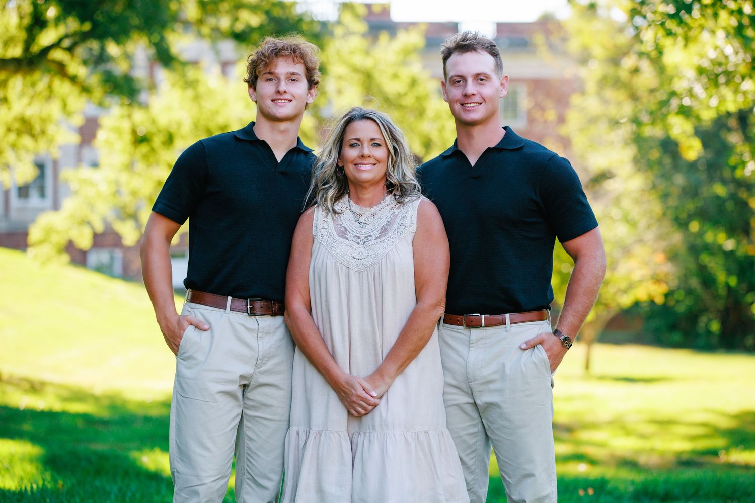 Family portrait of three people in matching black polos and khaki pants on sunny lawn.