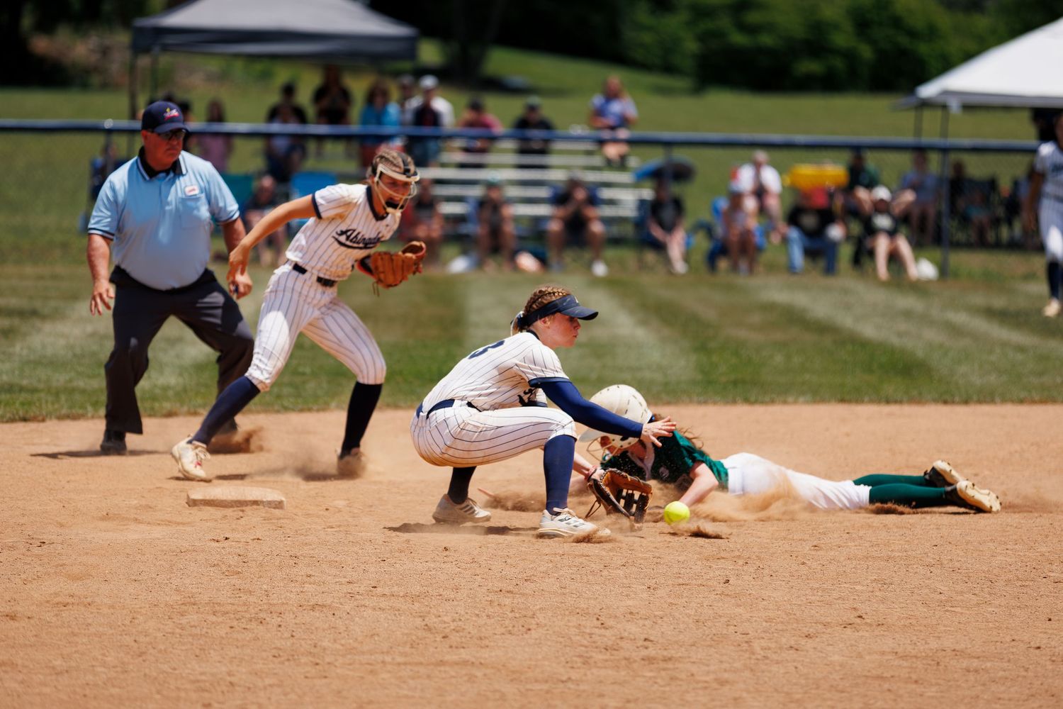 Softball player slides into second base as fielder attempts tag during competitive youth game on sunny day.