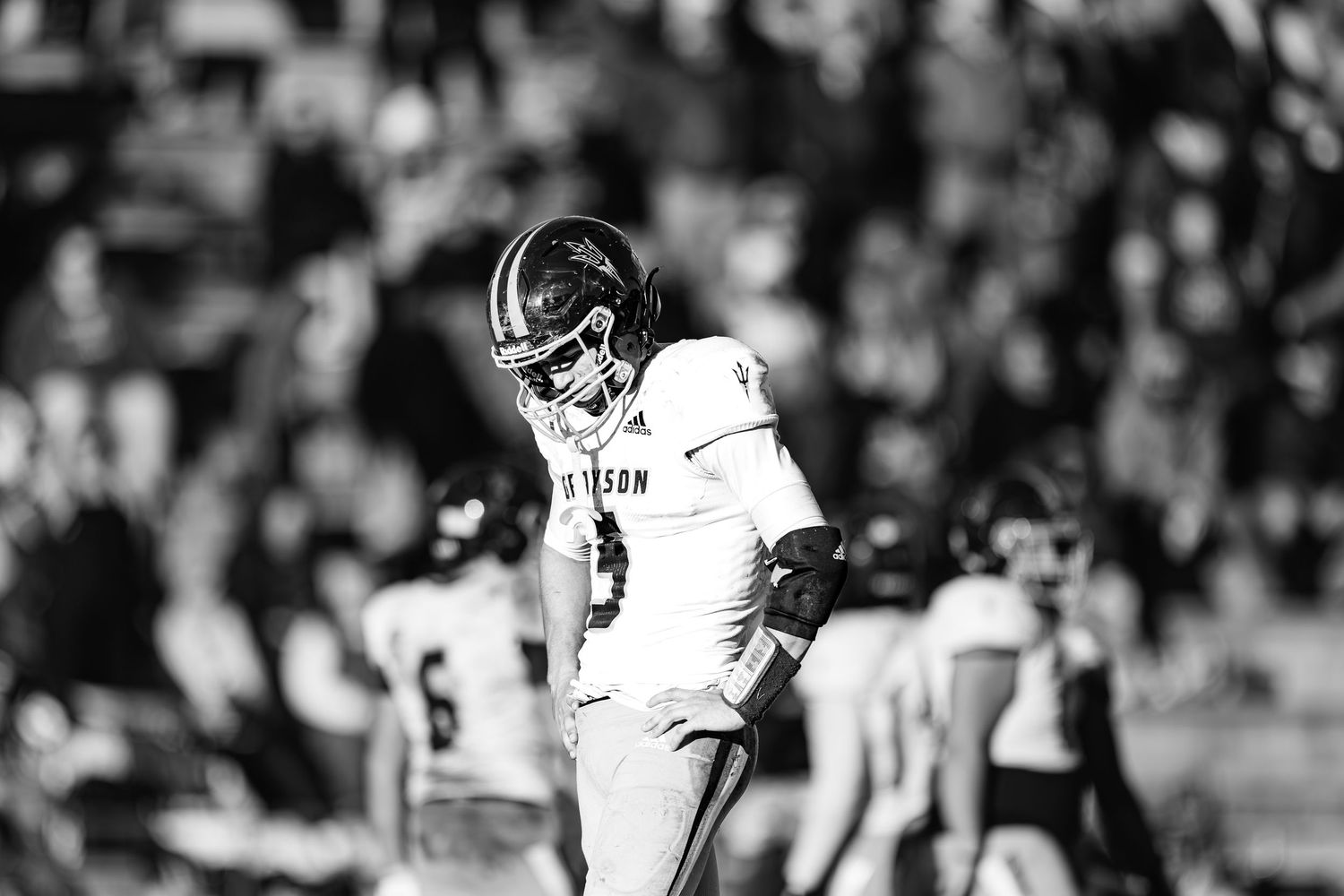 Football player in white uniform looks down during intense game moment in black and white.