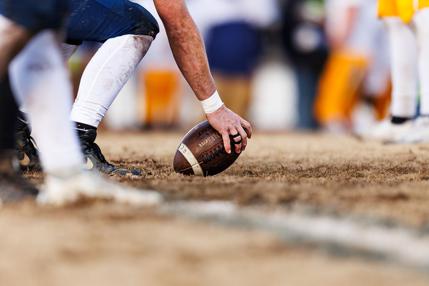 Close up of player's hand placing football on dirt field before snap.