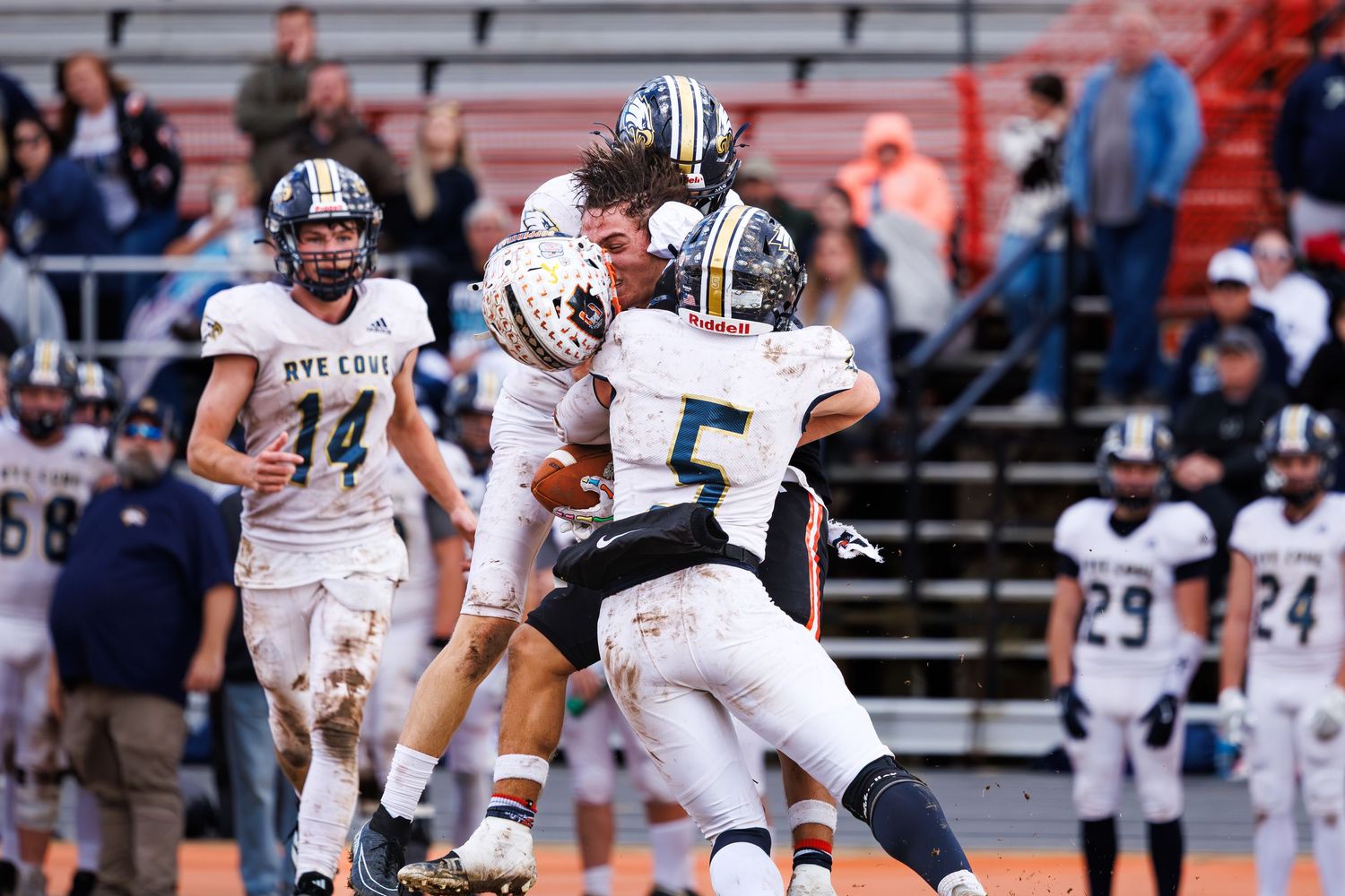 Football players in white and dark uniforms clash during a competitive game on the field.