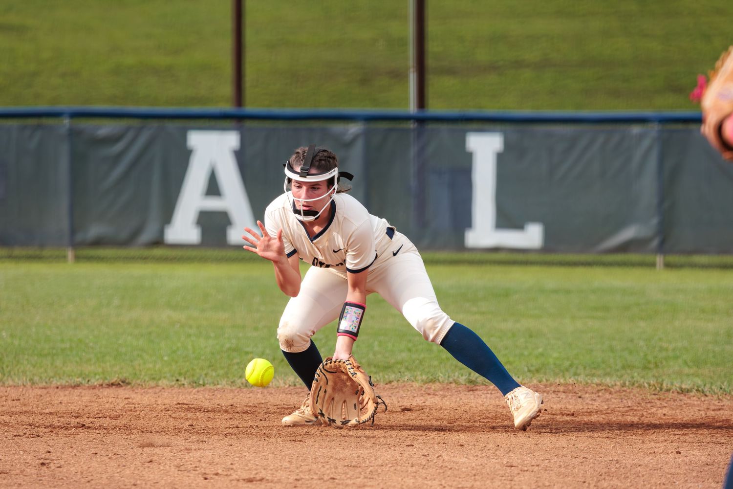 Softball player fields a ball in the infield to make the throw for the out at first.