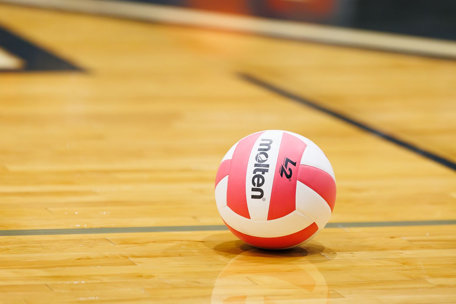 A Molten volleyball resting on a hardwood gym floor near the court boundary lines.