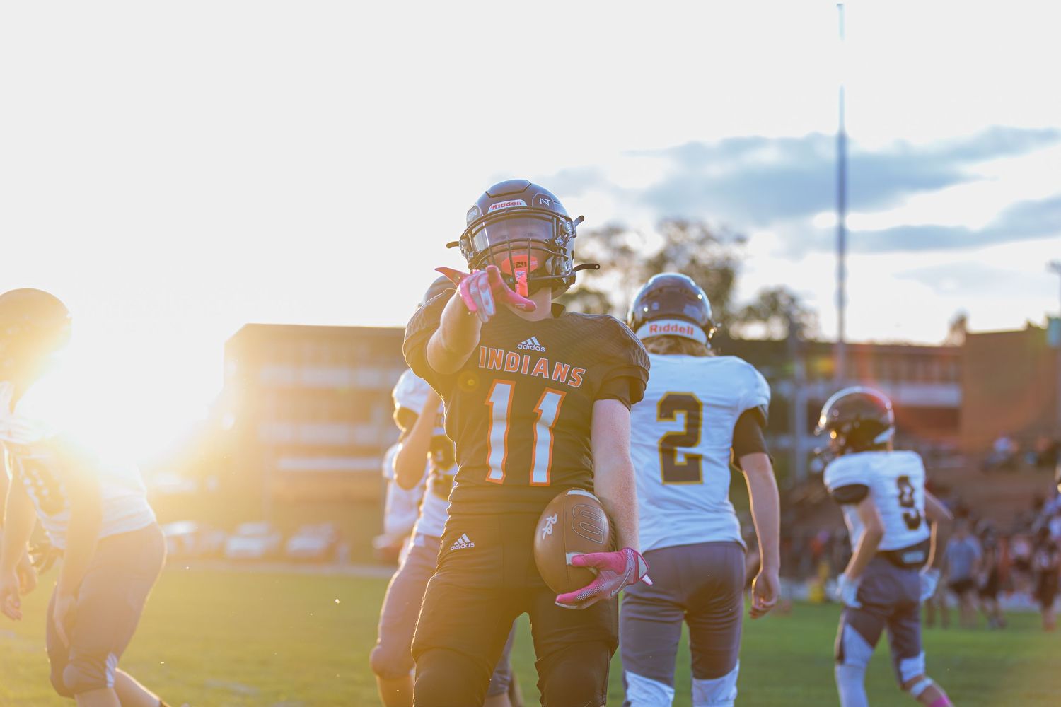 Football players practicing on a field during golden hour sunset with dramatic lighting.