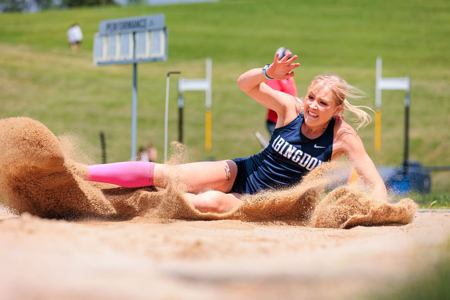 Track and field athlete performing a long jump at an outdoor competition, creating a splash of sand upon landing.